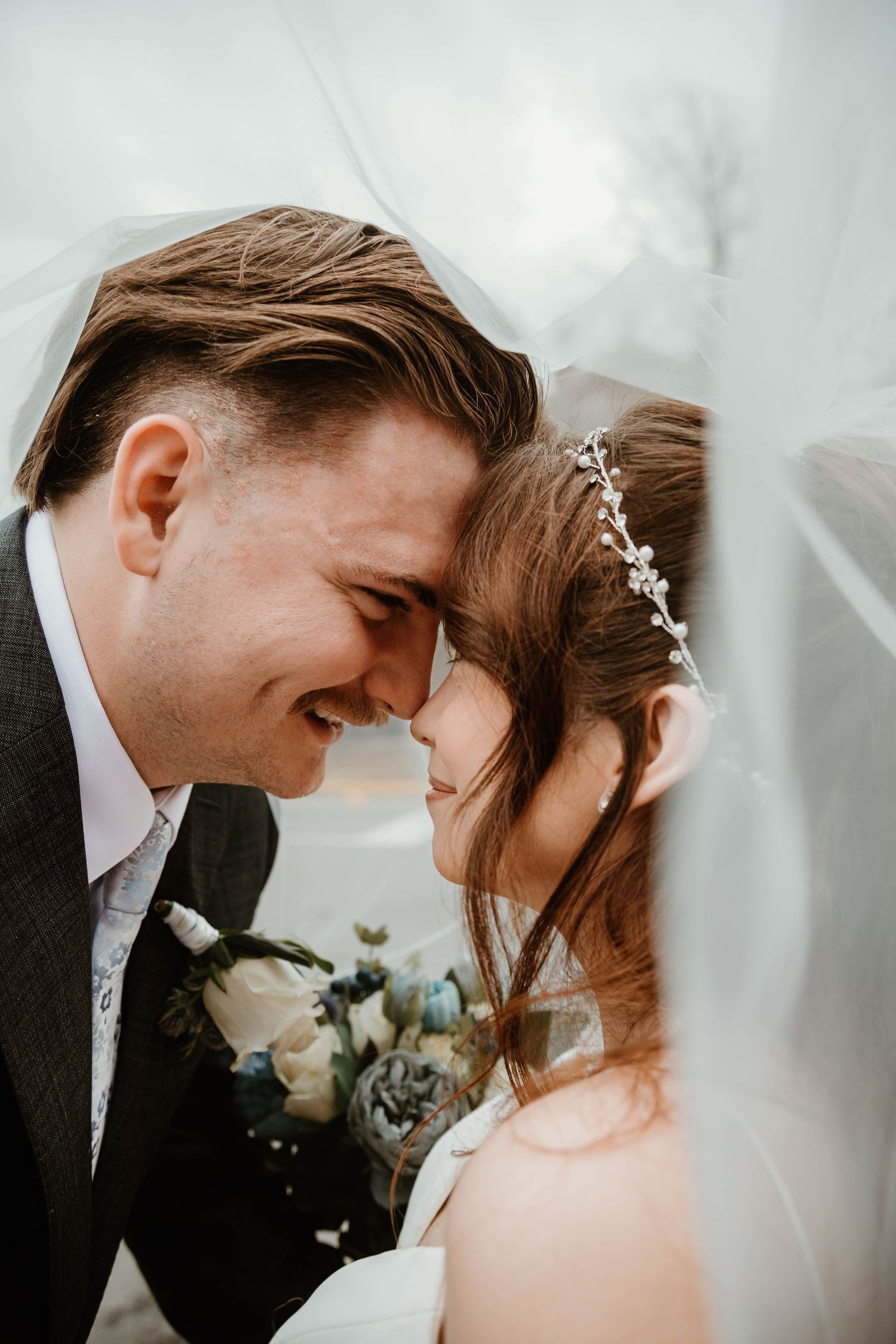 Bride and groom touching foreheads under veil, sharing a romantic moment on their wedding day.