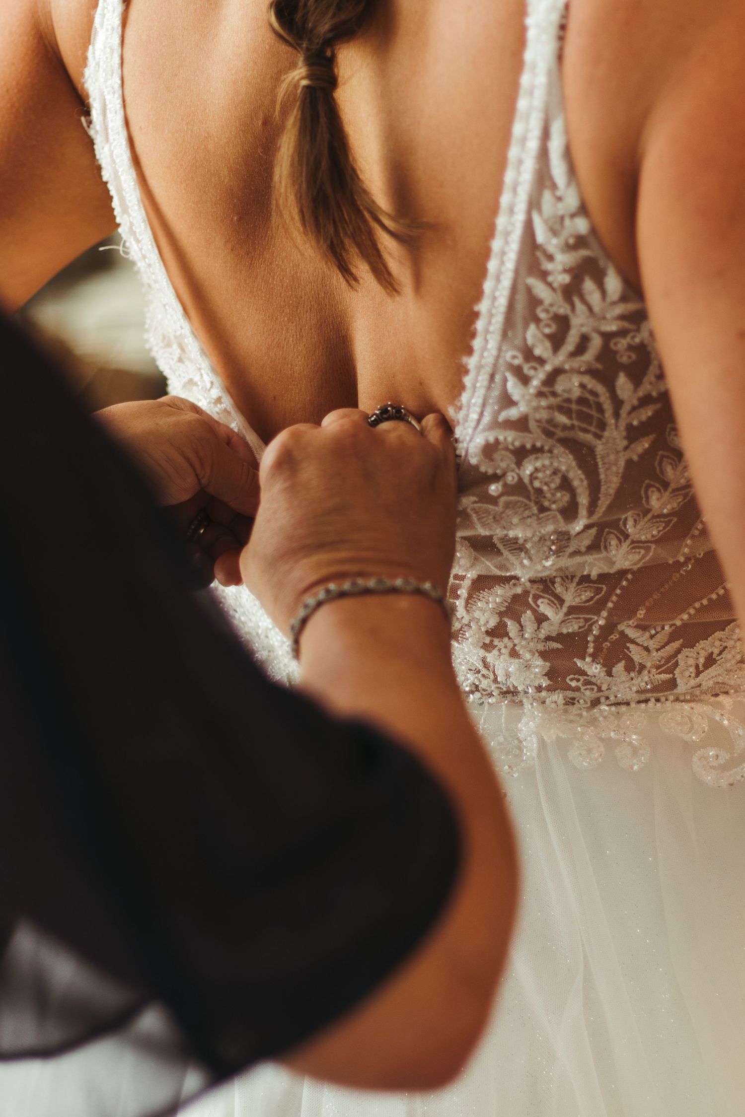 Close-up view of someone buttoning up the back of an intricate lace wedding dress with delicate details near Anderson, SC.