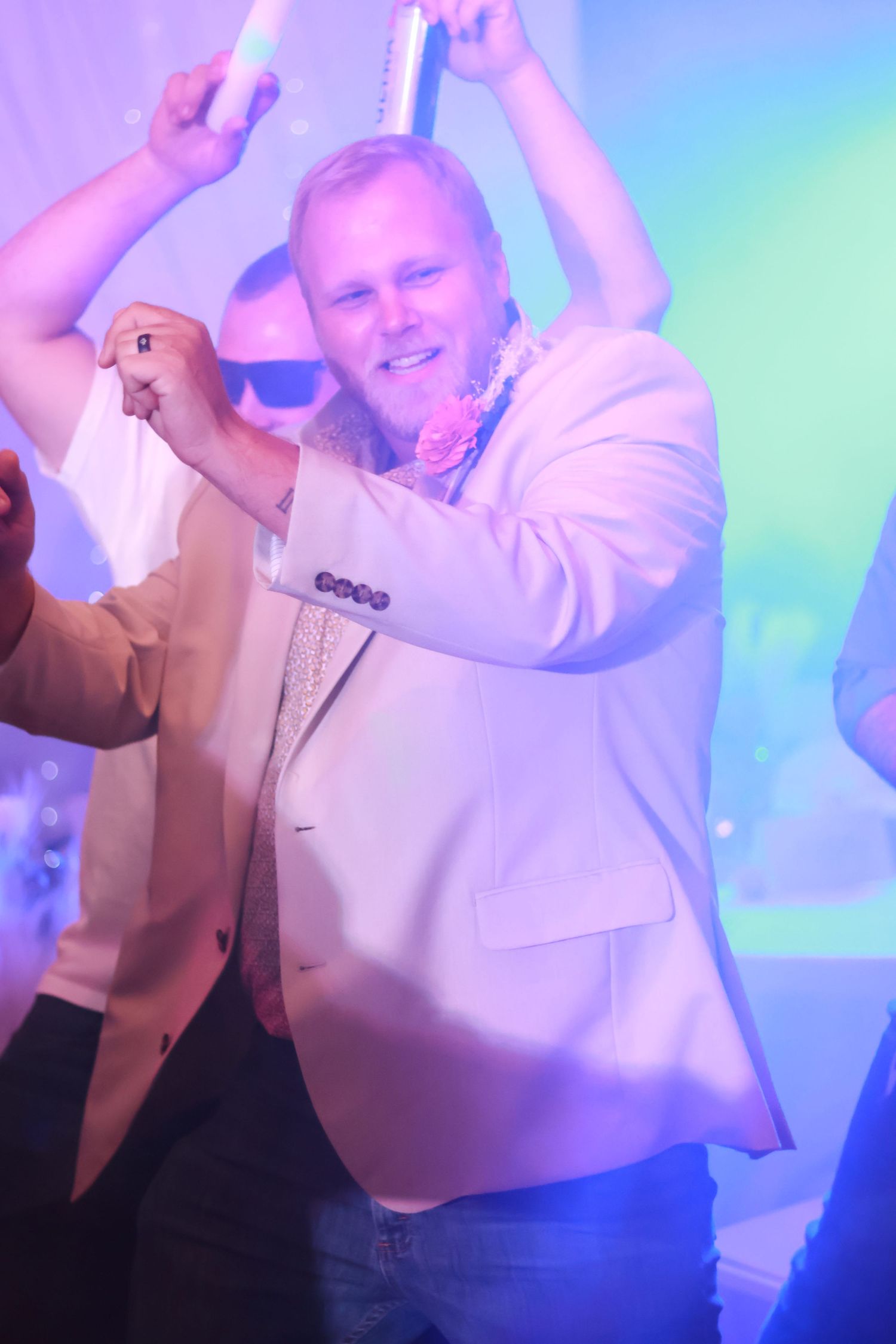 Someone wearing a white blazer dances at a wedding reception with colorful purple and blue lighting effects in background in Georgia.
