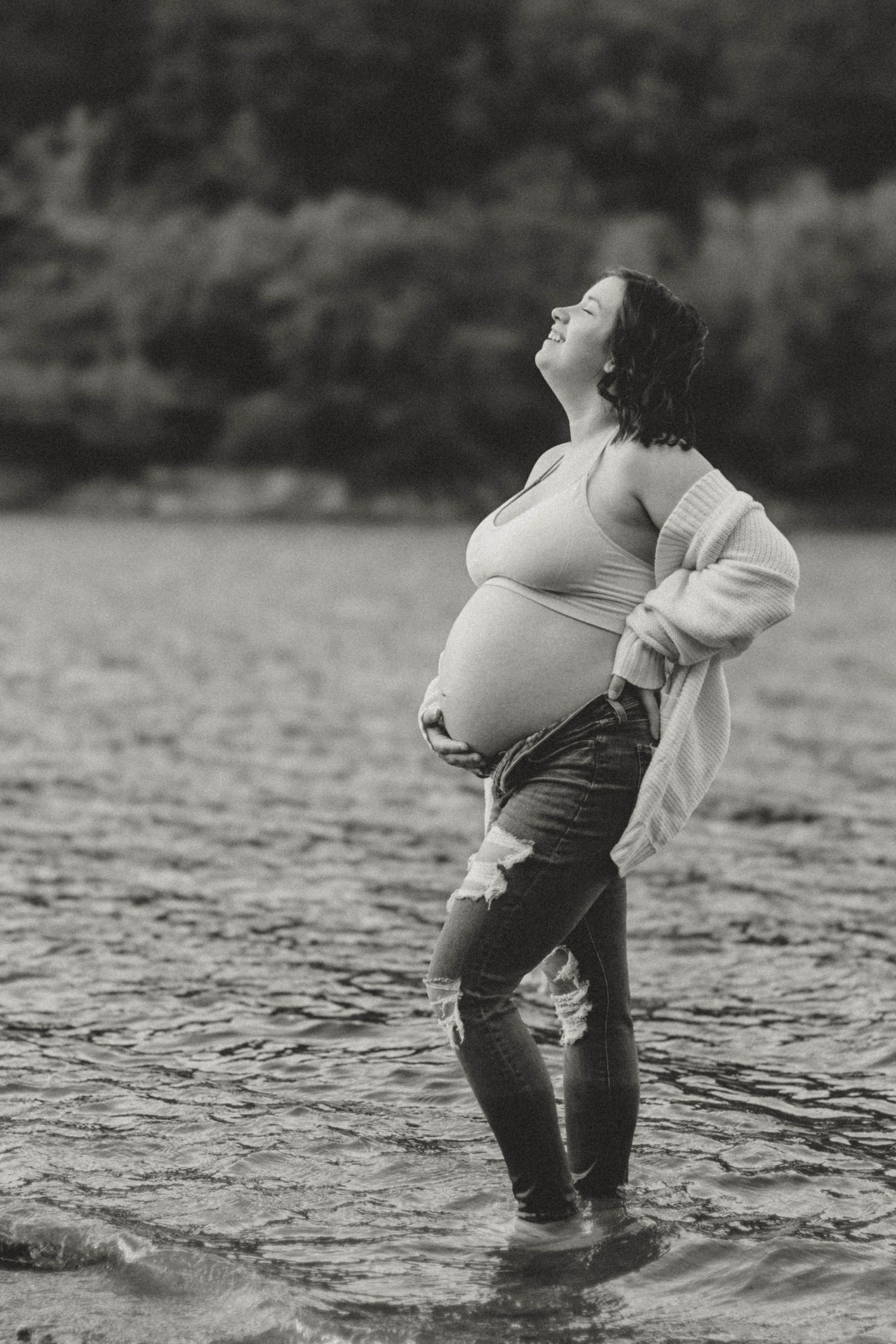 Black and white photo of a pregnant woman standing in water, arching her back with eyes closed in a peaceful moment at Broken Bridges.