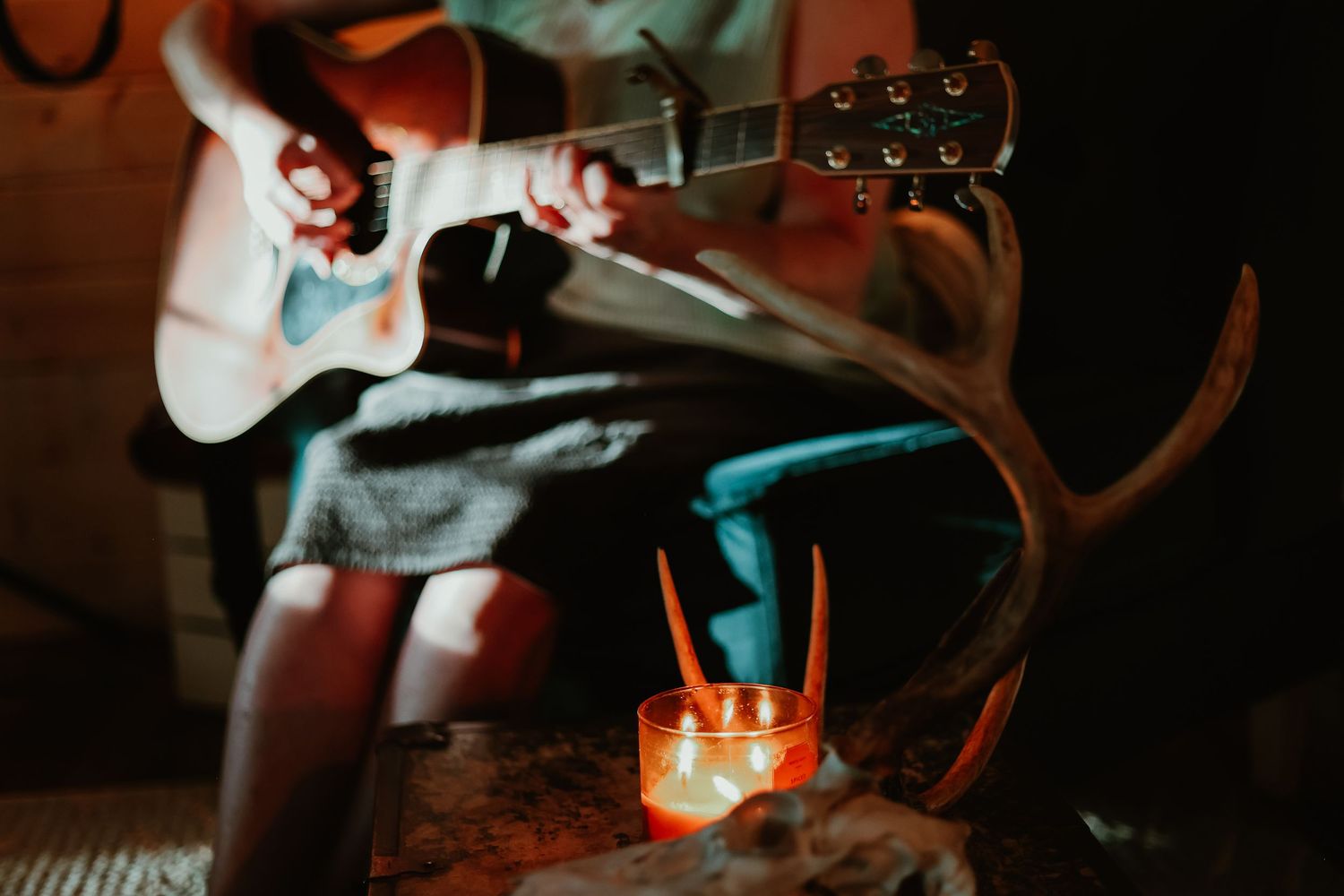 Person playing guitar by candlelight with antlers decorating the rustic setting in Georgia.