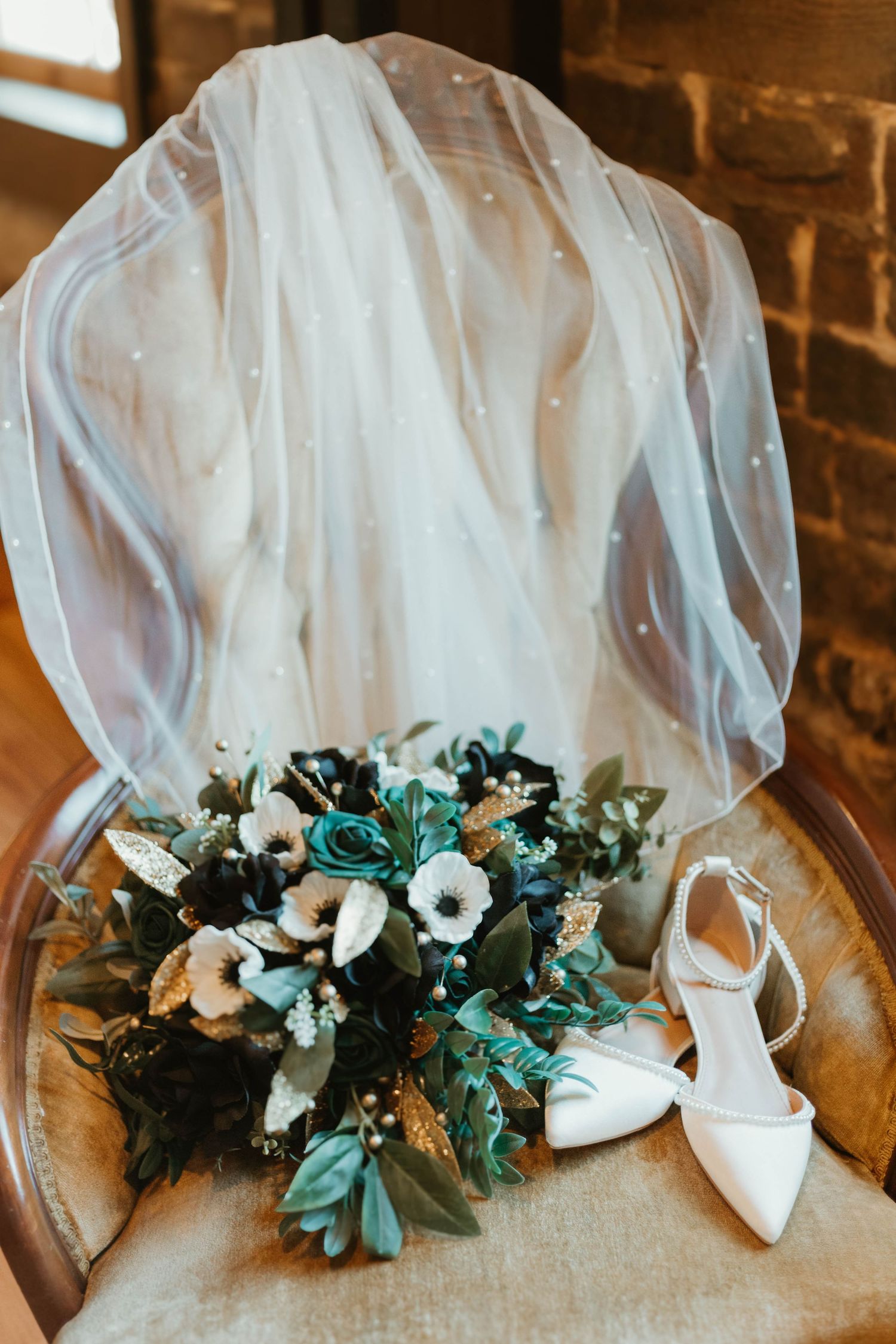 Wedding dress details with white shoes and delicate teal floral bouquet arranged on wooden flooring.