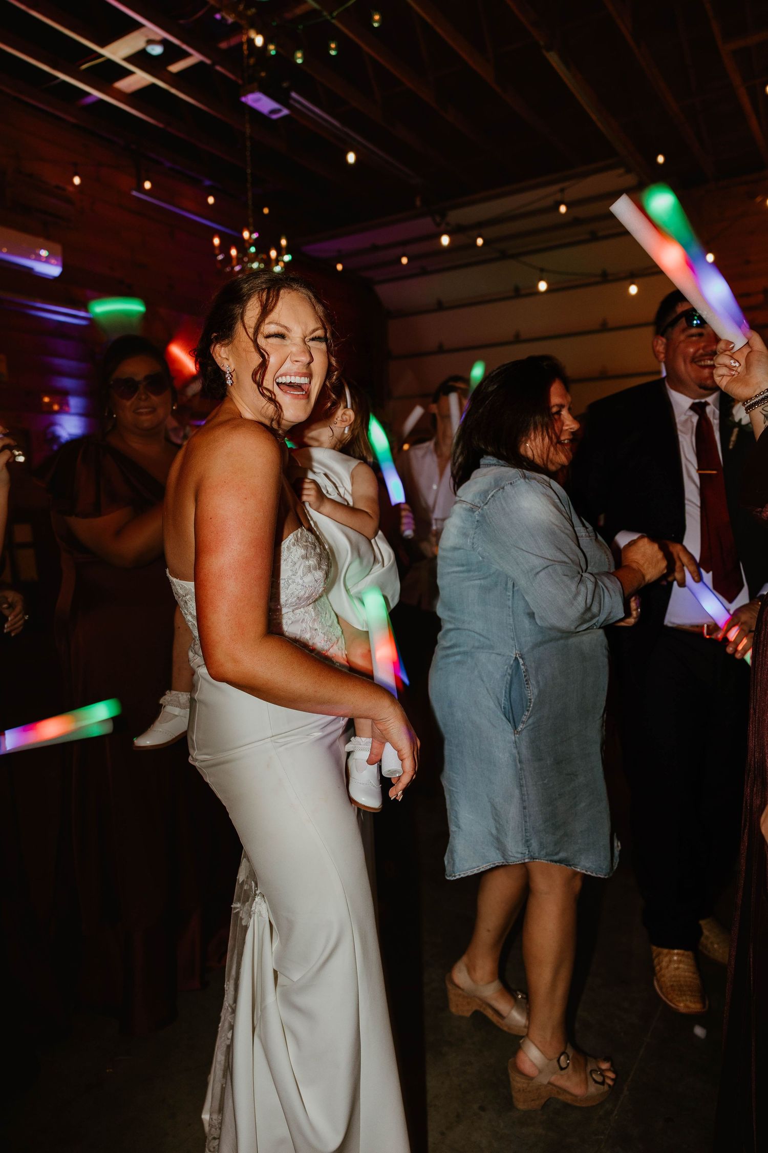 Wedding reception guests dancing under colorful disco lights in a dark venue.