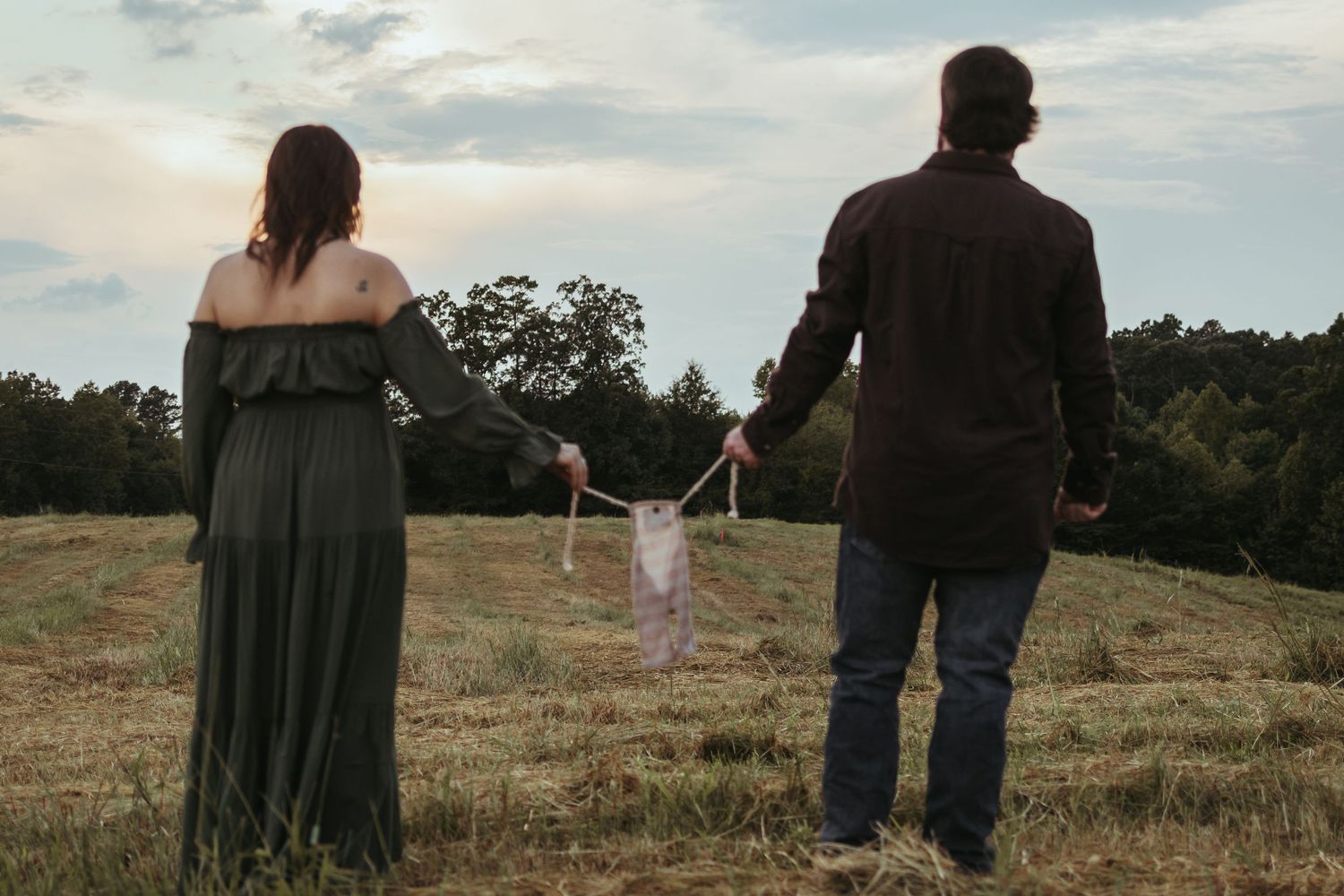 A couple holding hands while standing in a sunset-lit field with flowing fabric for a maternity session near Clarkesville, GA..