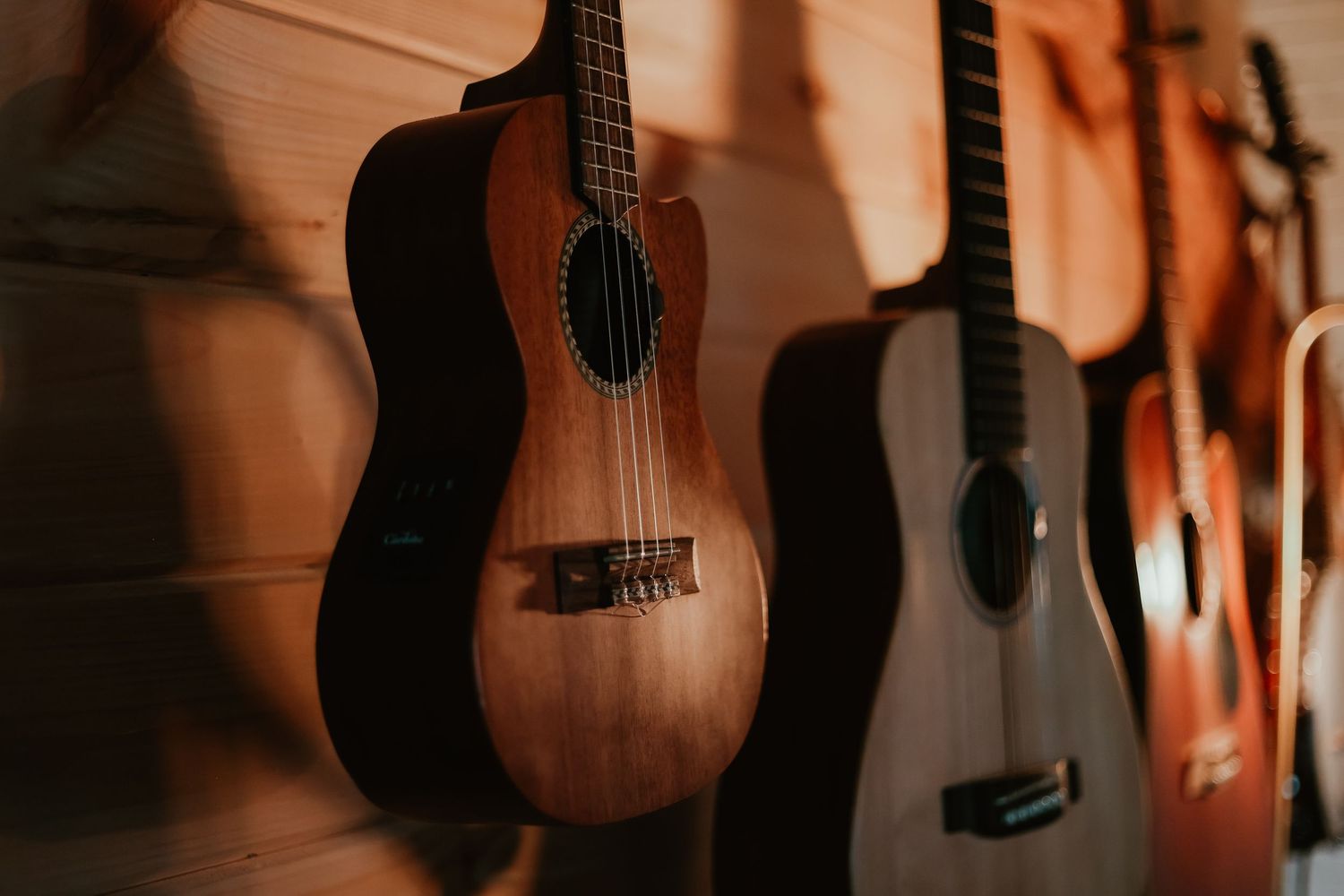 Multiple acoustic guitars hanging on a wooden wall in warm lighting at a home in Toccoa.