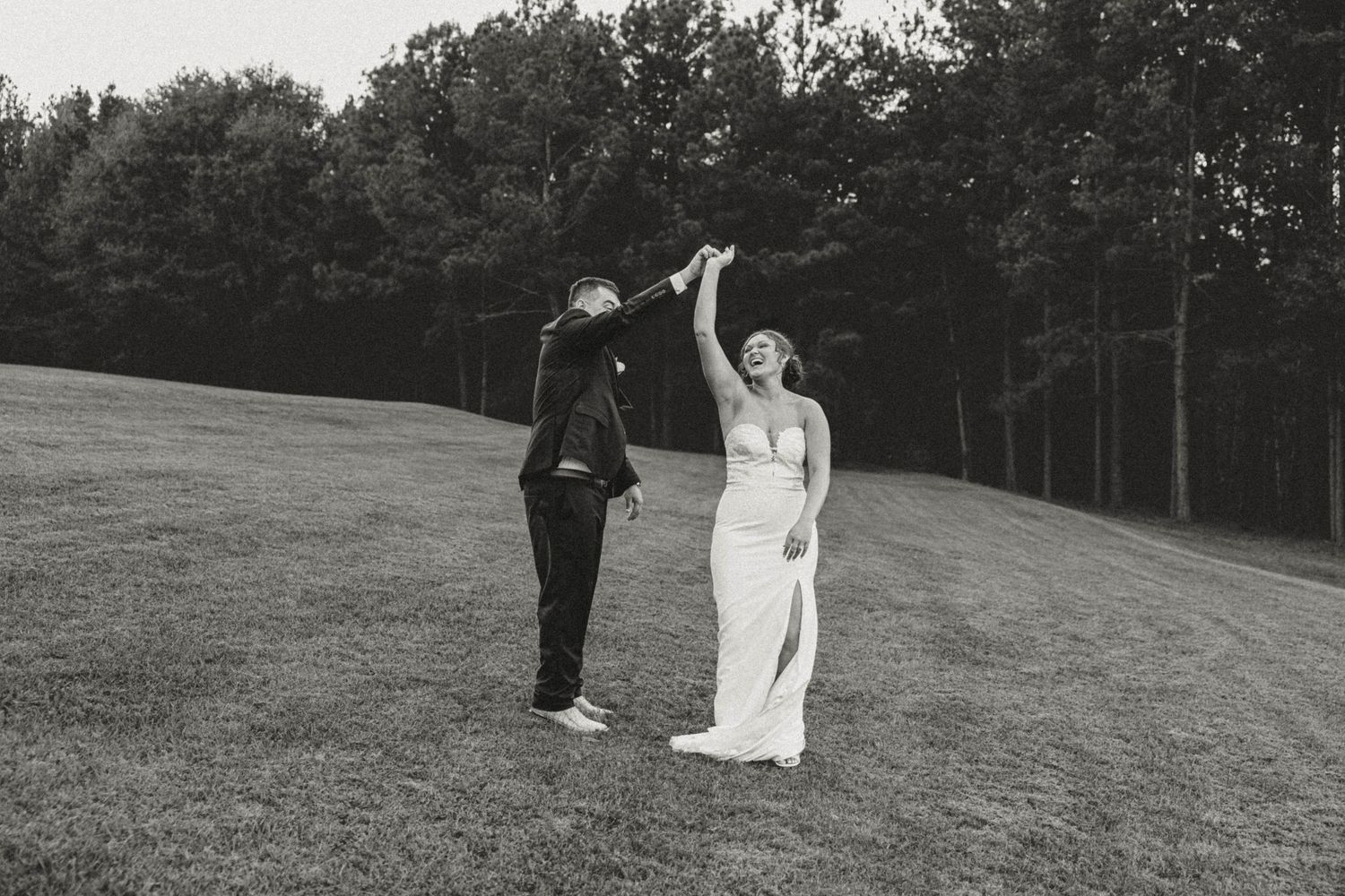 A couple dances together on a grassy hill during their wedding celebration.