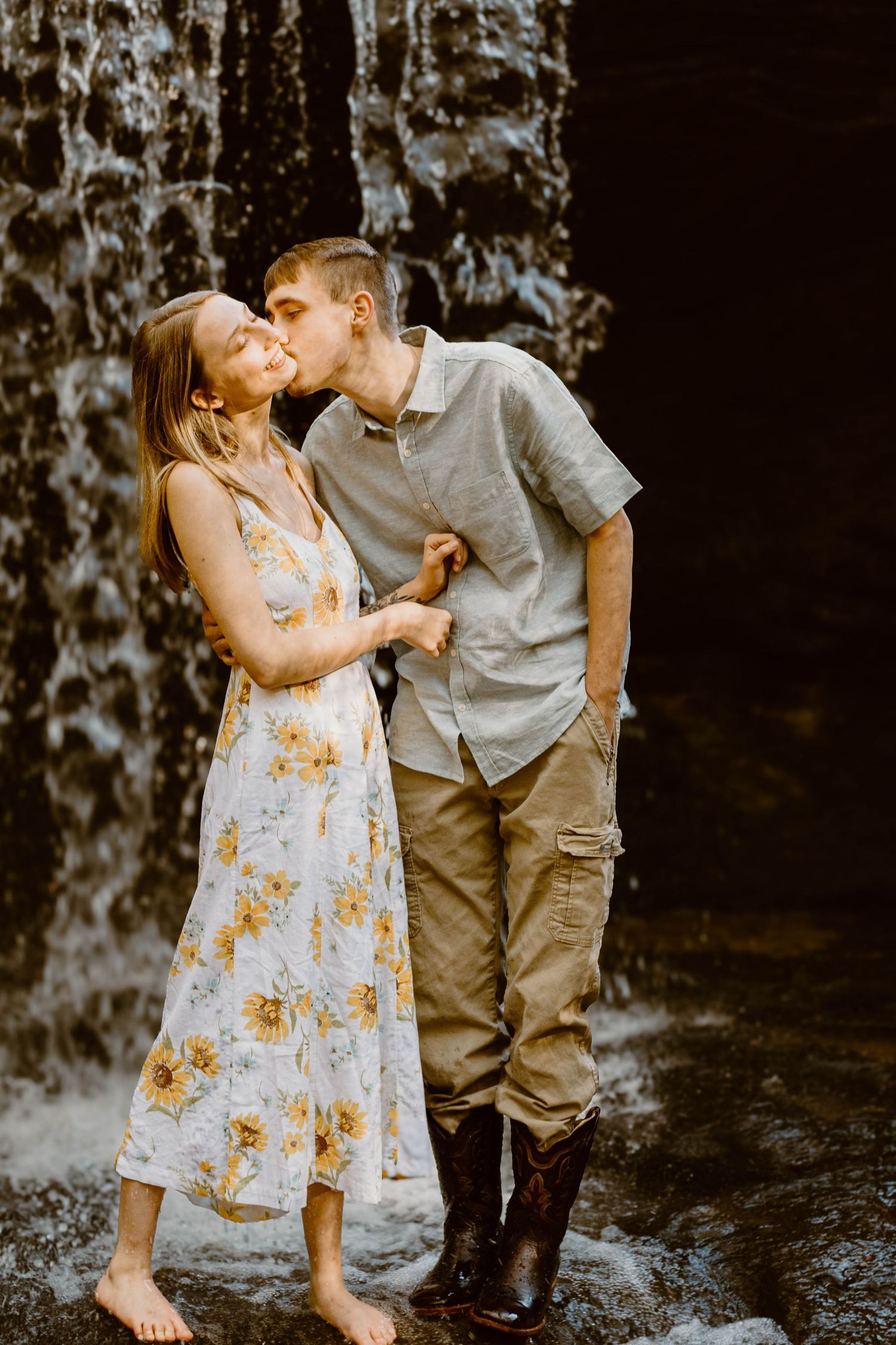 Romantic couple sharing a kiss by cascading waterfall with sunlit glow in nature setting at Henderson Falls in north Georgia.
