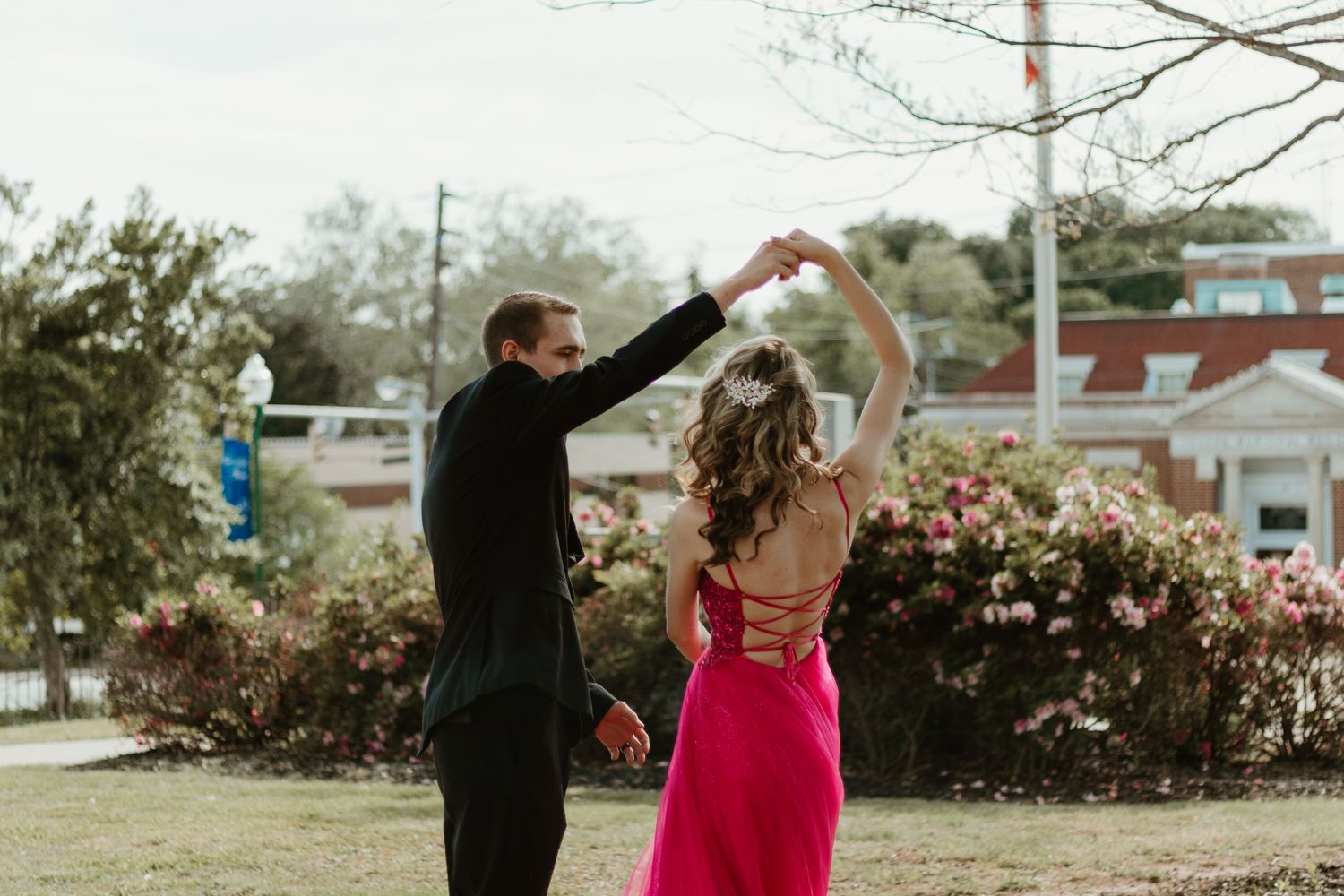A couple dances outdoors in formal attire with a pink gown and black suit against flowering bushes in downtown Toccoa.