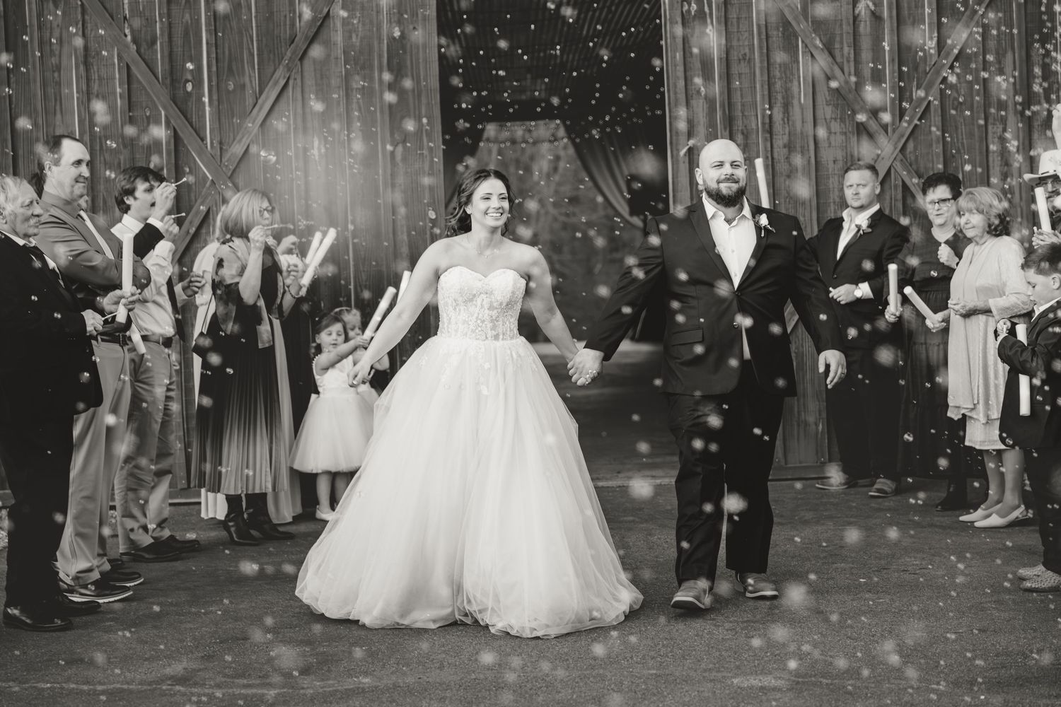 Black and white photo of a bride and groom exiting their wedding ceremony through a shower of confetti.