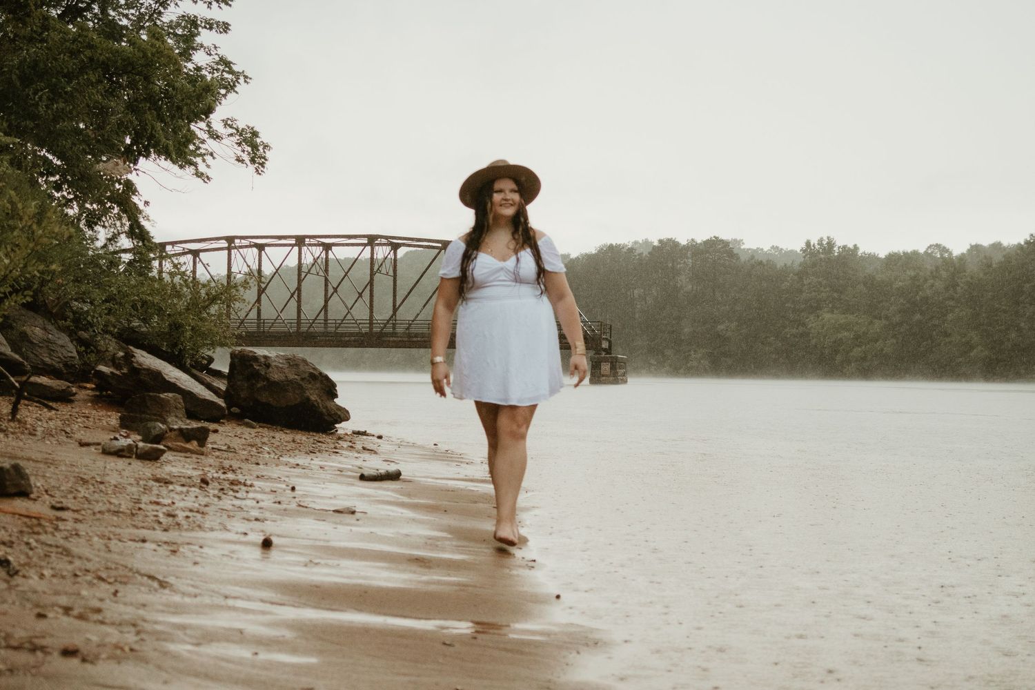 A figure strolls barefoot along a sandy lake beach on a misty afternoon near Broken Bridges on Lake Hartwell.