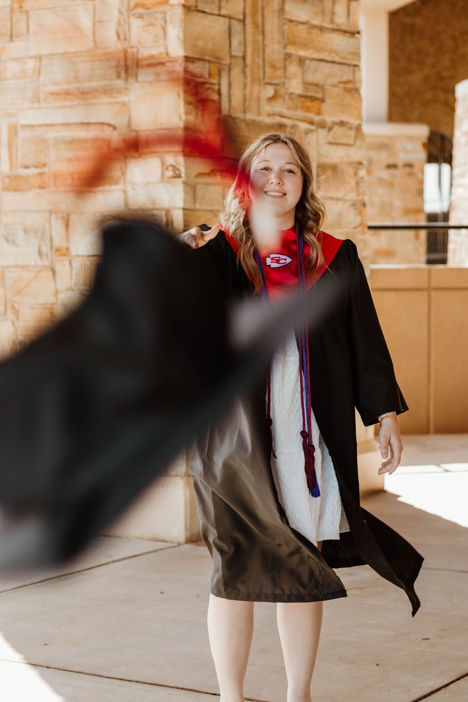 A graduate in academic regalia poses while their cap is tossed in motion at Stephens County High School in northeast Georgia.