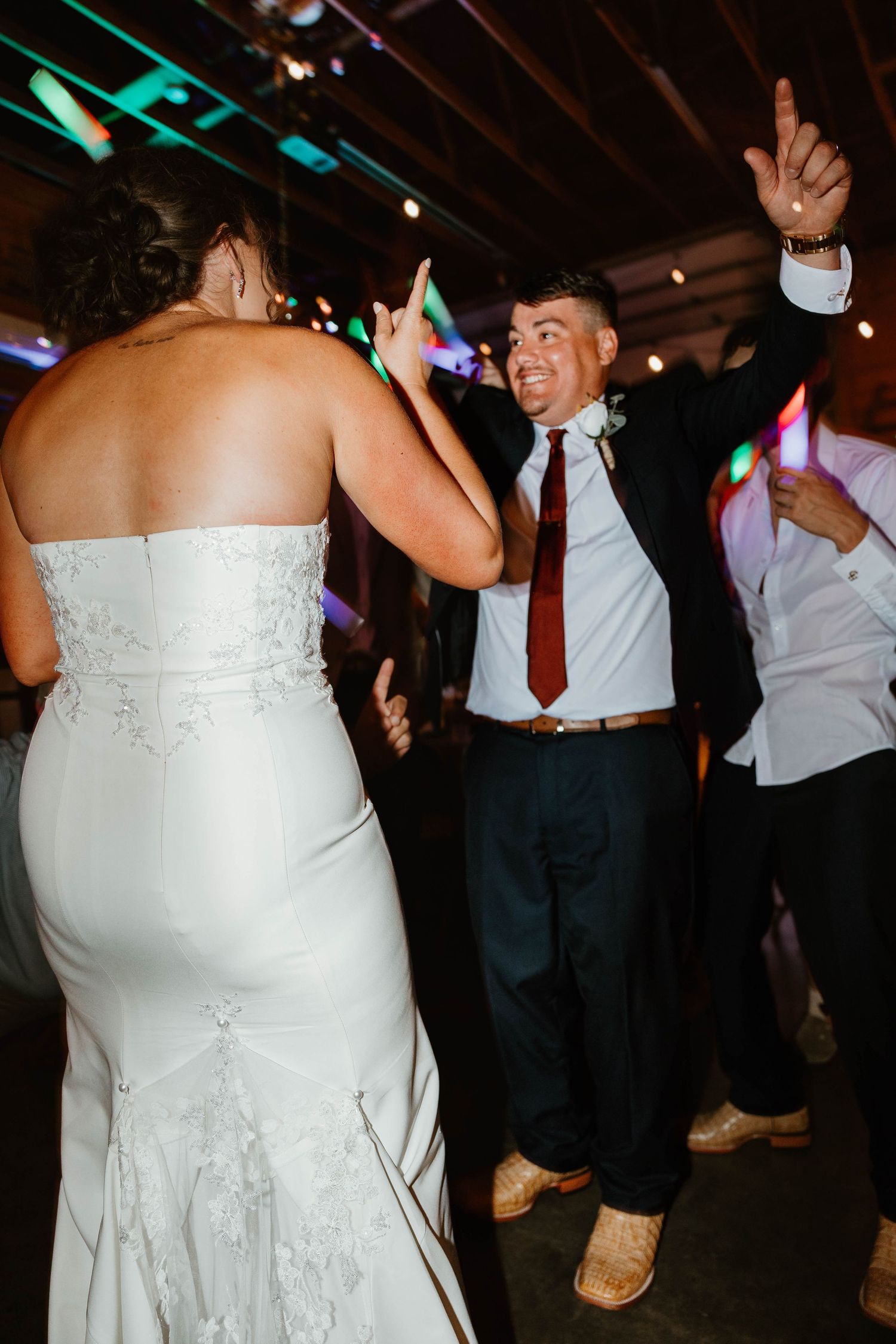 Wedding celebration on dance floor with bride in white dress and guests dancing under party lights.