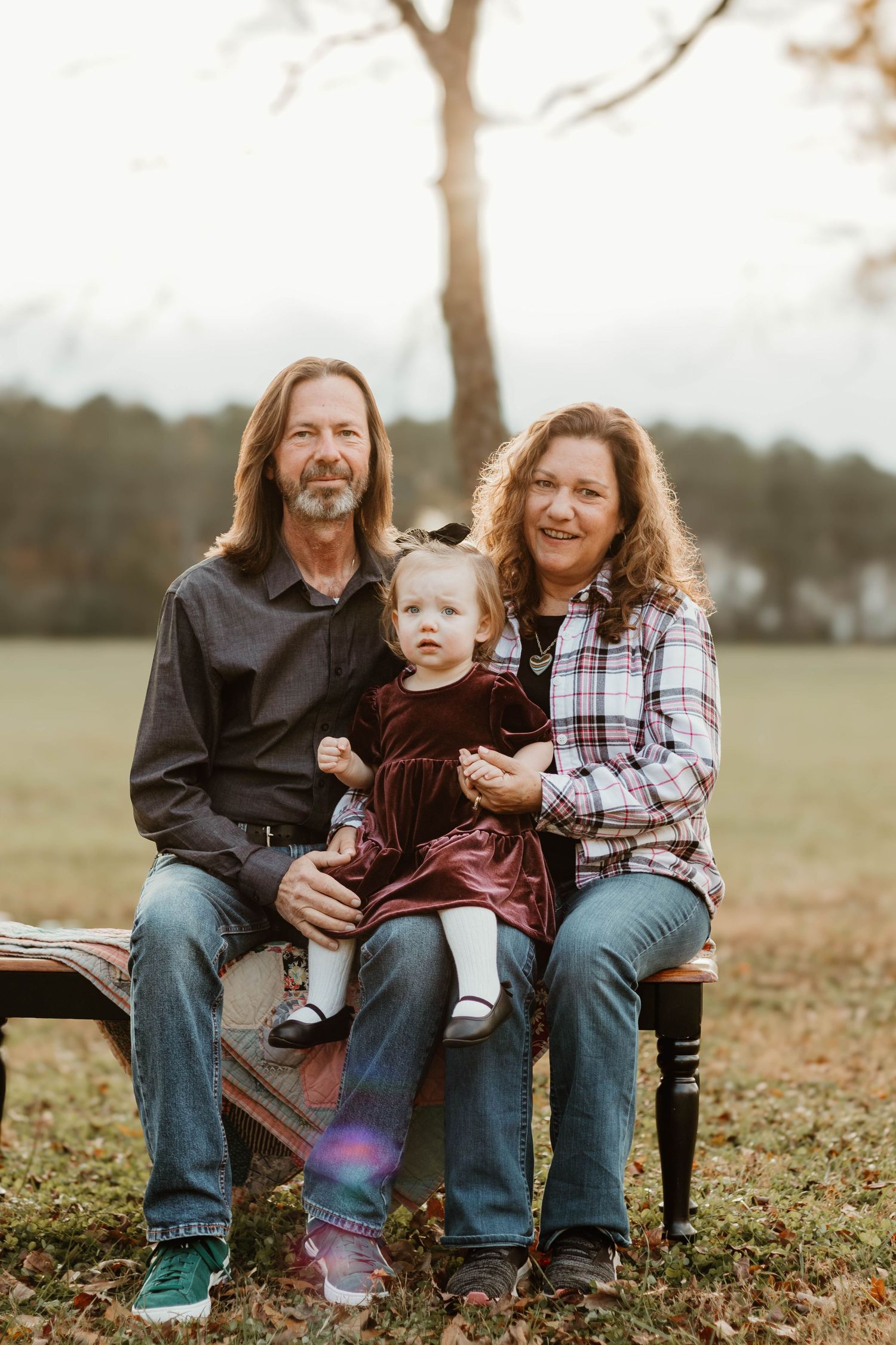 Joyful family sharing laughs while seated on wooden bench in autumn field setting in northeast Georgia.