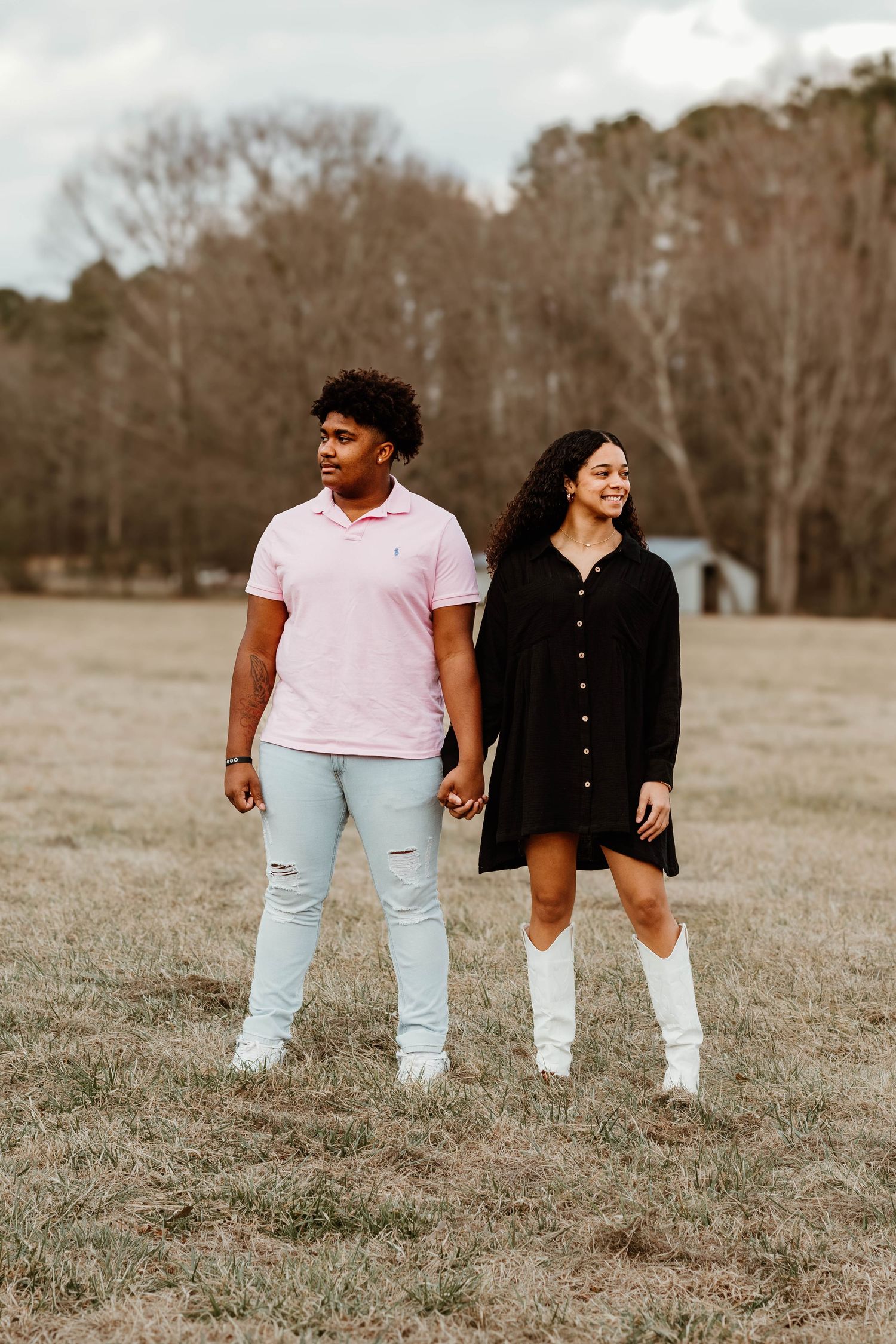 A couple holds hands while standing in an open field wearing contrasting light and dark outfits in Toccoa, GA.