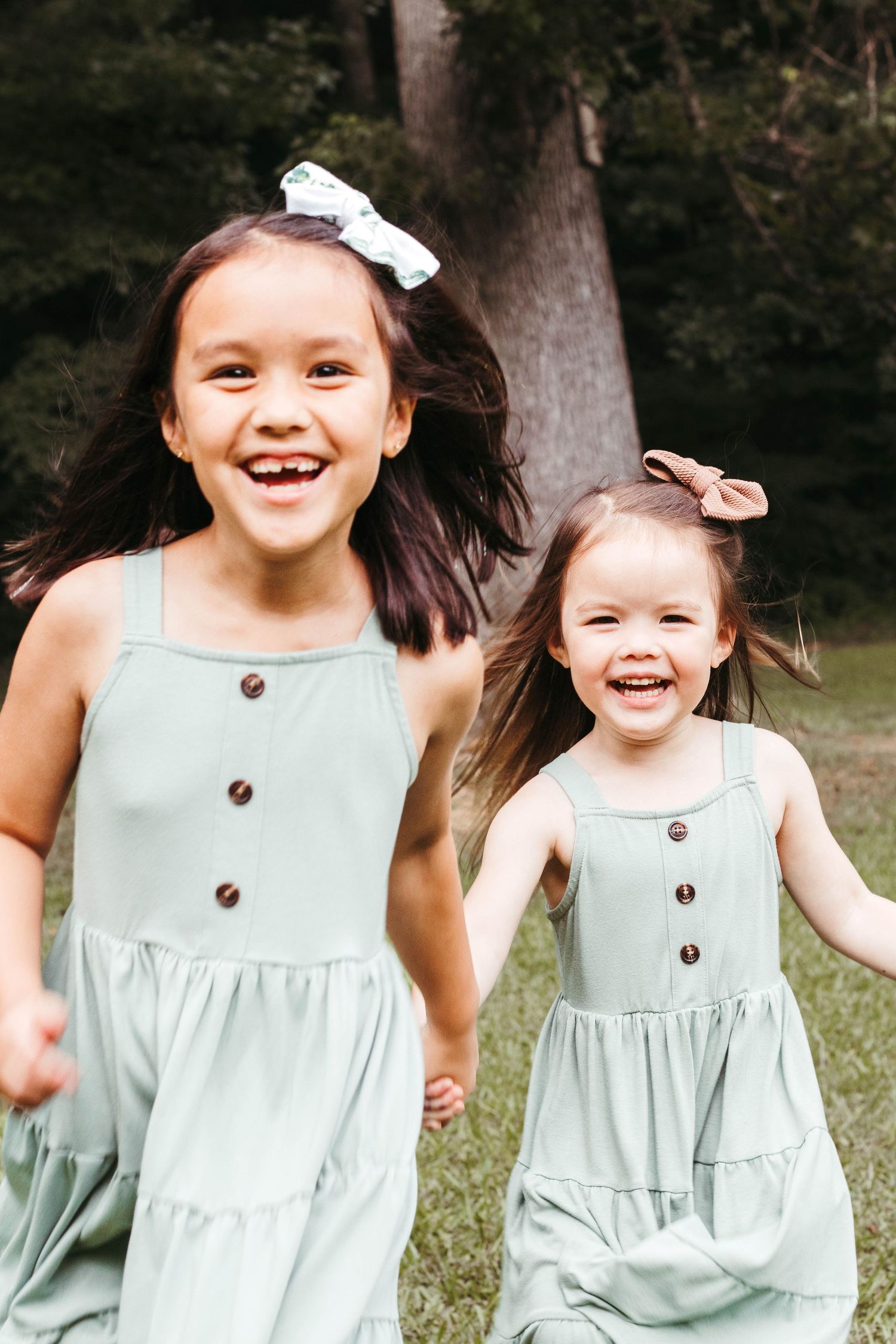 Children wearing matching mint green dresses with buttons laugh and play together in a natural outdoor setting.