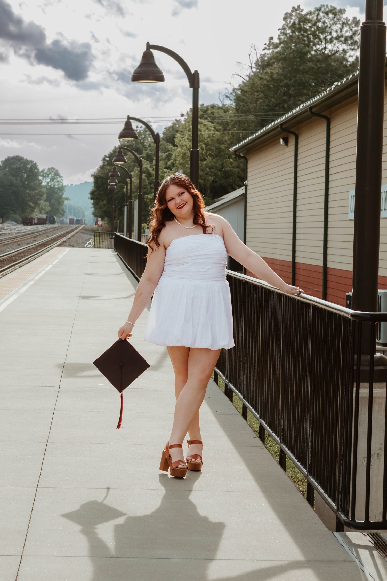 Graduate in white dress poses with diploma on a platform near train tracks in northeast Georgia.