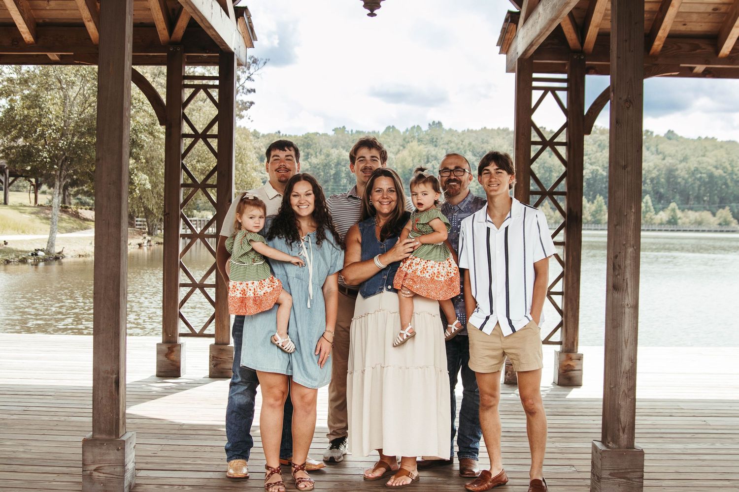 Family portrait session captured under a rustic wooden pavilion by the waterfront during golden hour.