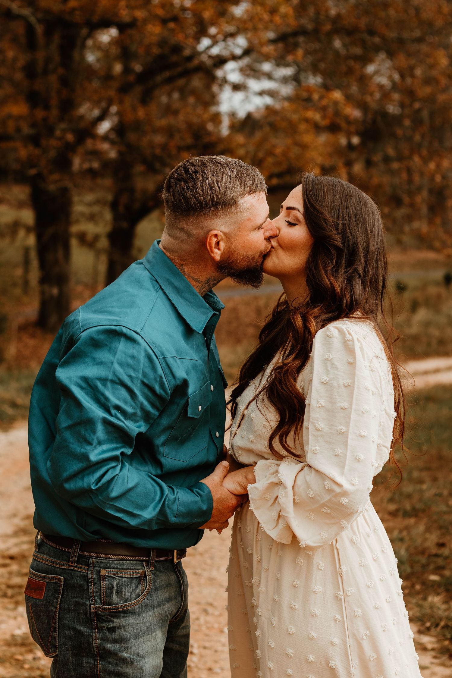 Romantic couple shares tender moments in a fall setting wearing coordinating cream and teal outfits in Northeast Georgia.
