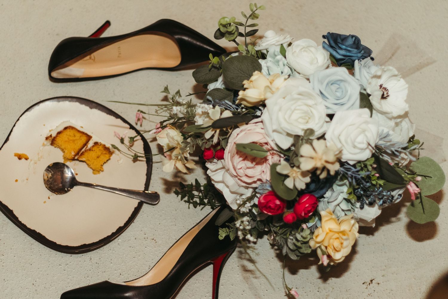 Wedding shoes surrounded by delicate floral arrangements with white roses and soft blue accents on a light surface in Greenville, SC.