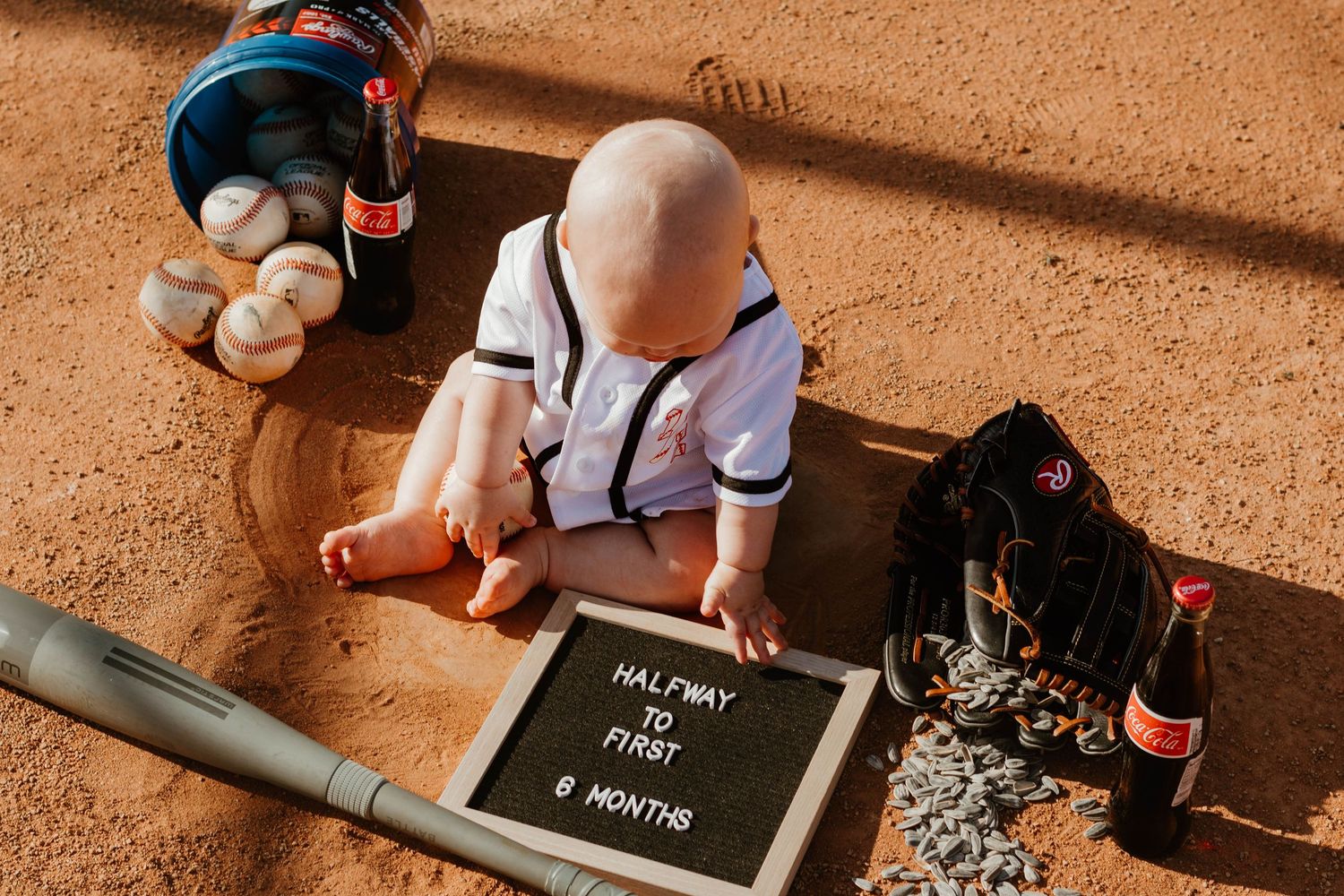 Overhead view of baby with baseball milestone sign and sports equipment on ground in Toccoa, GA.