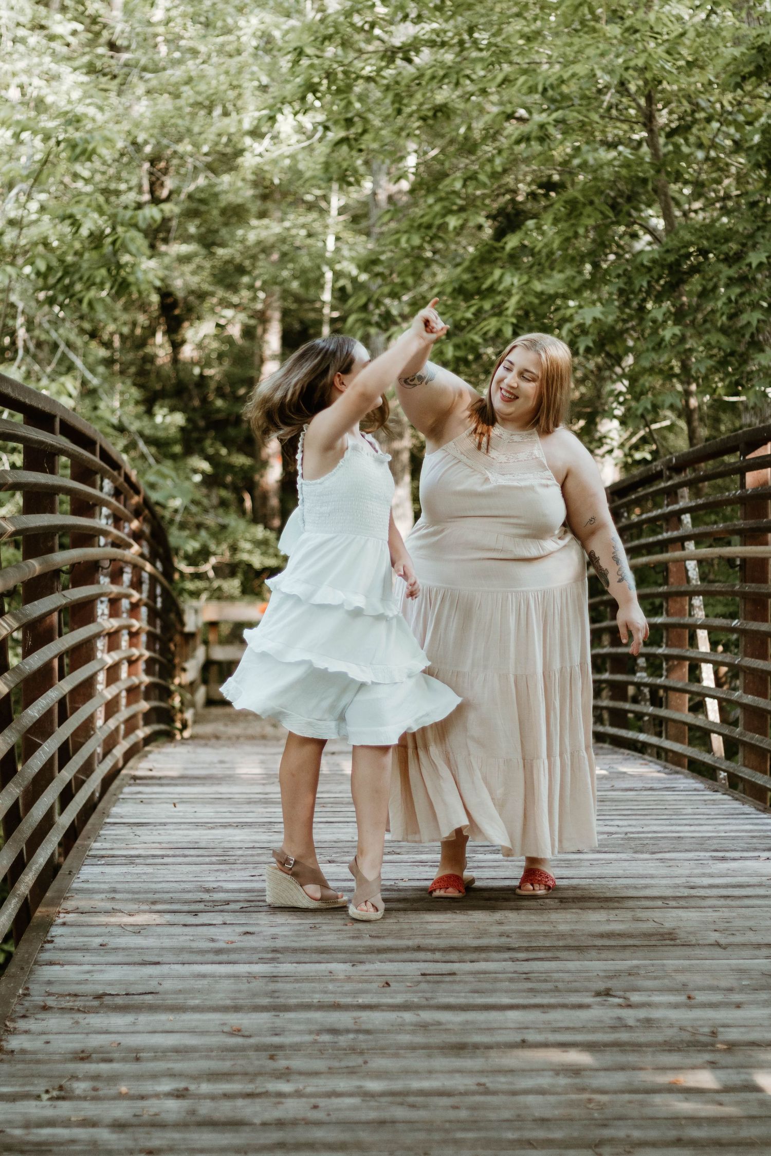 People in light colored dresses pose playfully on a wooden bridge surrounded by greenery at Victoria Bryant State Park in northeast Georgia.