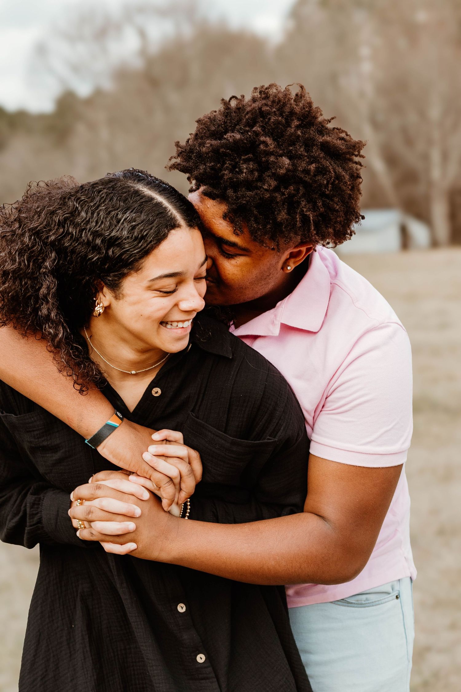 A couple shares an intimate embrace while laughing together in a sunlit field at Geary Farm in Toccoa, GA.