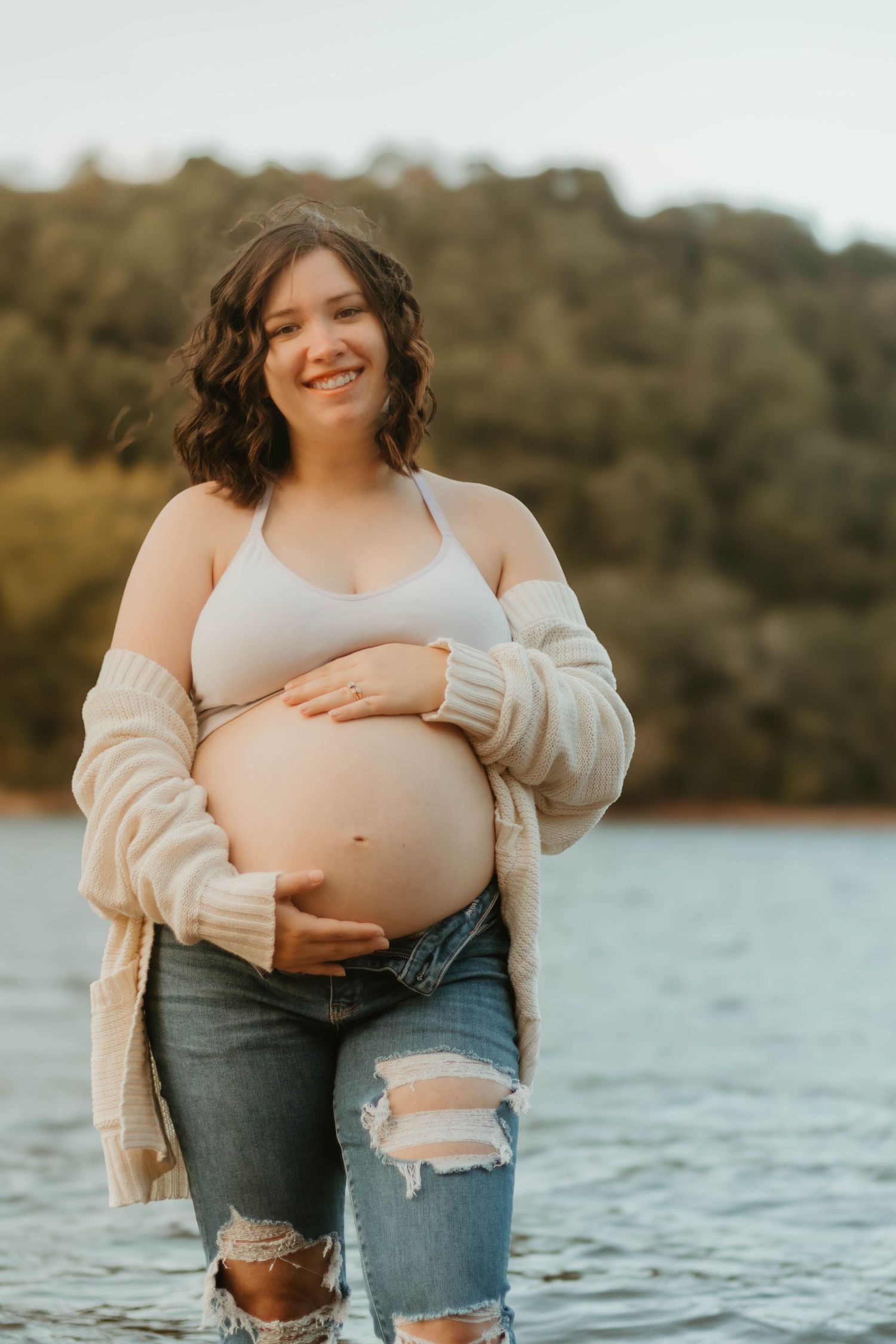 Joyful maternity portrait by Lake Hartwell showing pregnant belly in casual attire with cream cardigan.