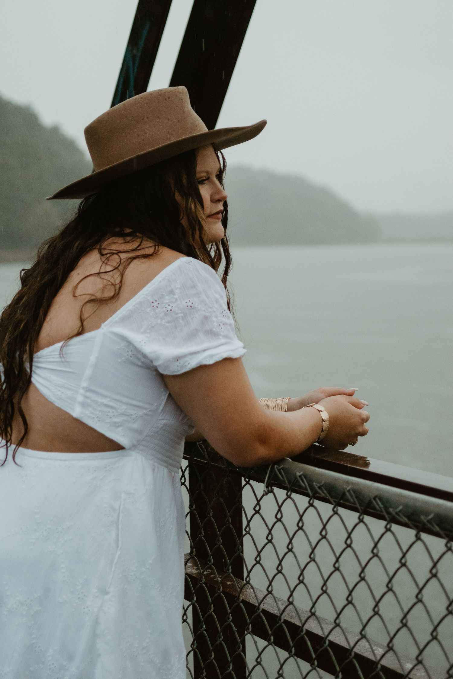 Person in white dress and brown hat leaning on fence overlooking misty Lake Hartwell.