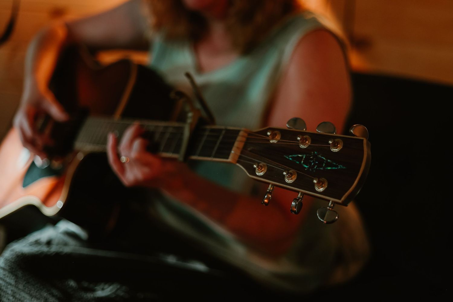 Close-up shot of hands playing acoustic guitar strings in dim lighting at a home in Northeast Georgia.