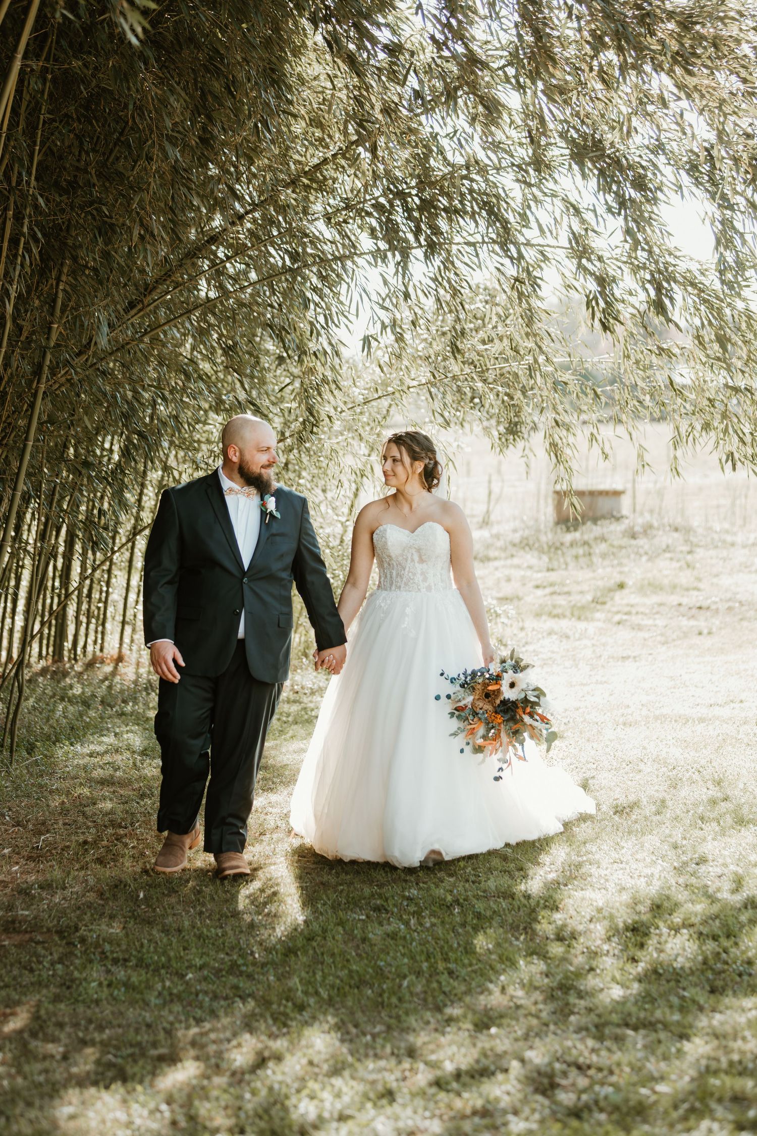 Bride and groom walk hand-in-hand under bamboo trees in outdoor wedding portrait.