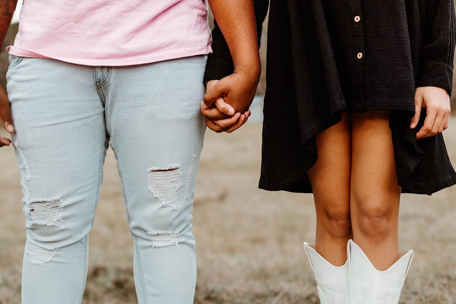 Close up view of two people holding hands, one wearing distressed jeans and another in a black dress with white boots in Toccoa, Georgia.