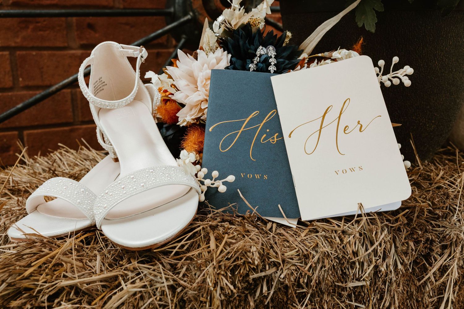 Wedding details including white shoes, calligraphy cards, and delicate snowflake decorations arranged on rustic hay.