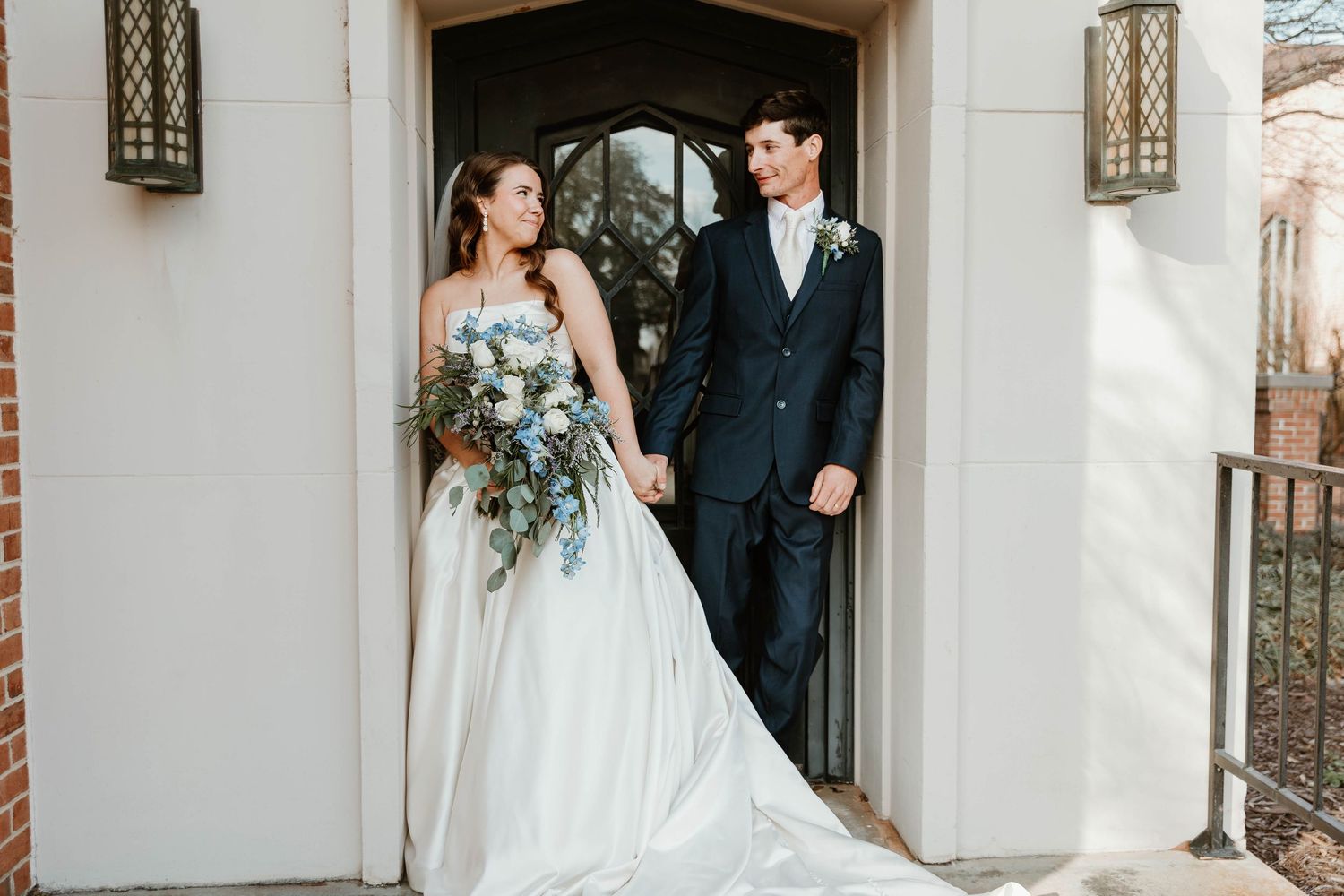 A bride and groom share intimate moments along a white wall with elegant lanterns and architectural details.