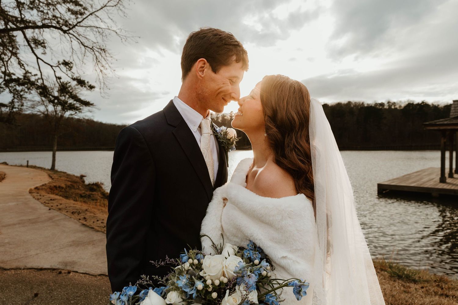A romantic couple in wedding attire embraces on a scenic beach at sunset during their coastal wedding celebration.