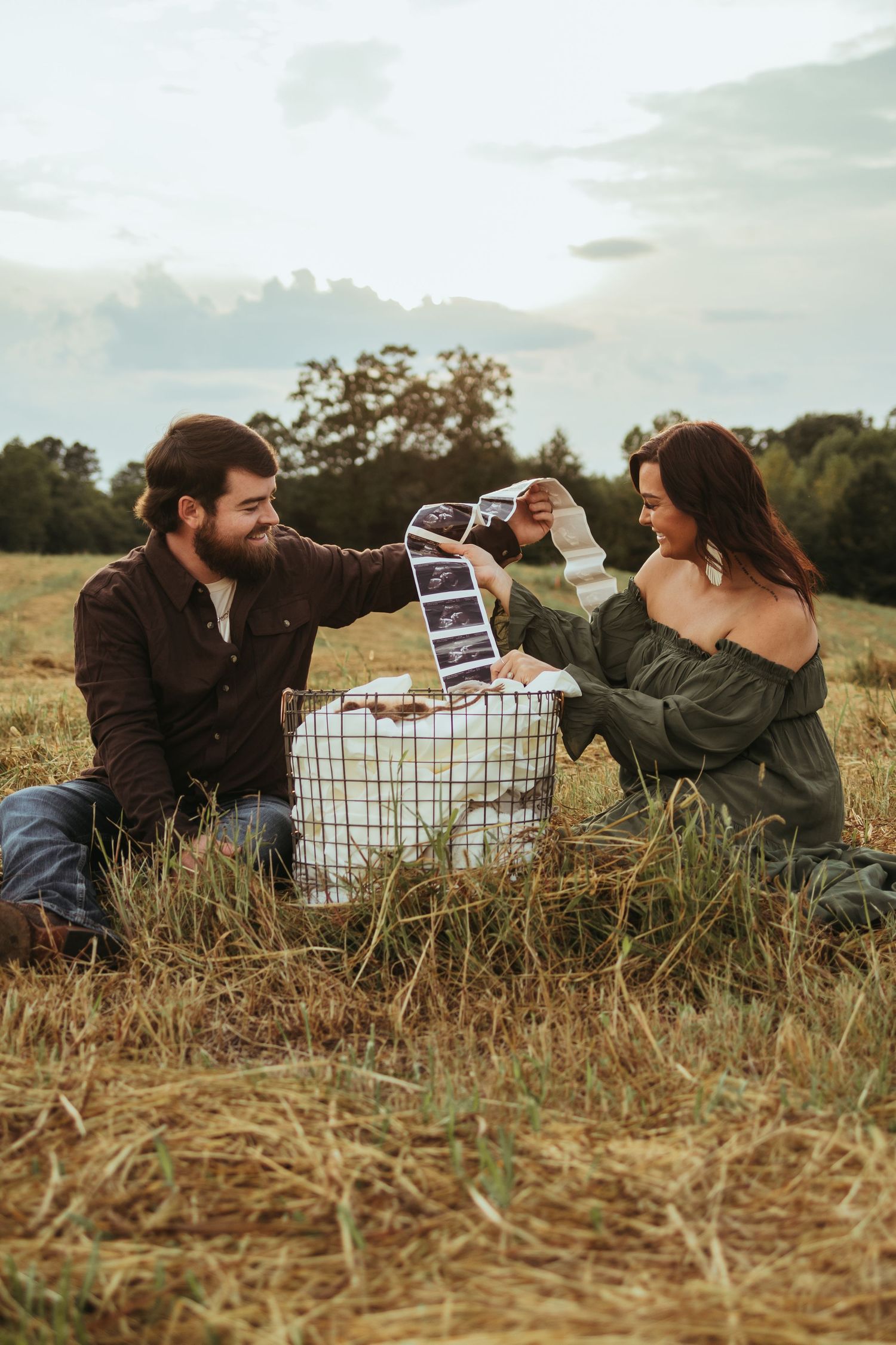A couple holding sonogram photos while sitting in a grassy field during sunset maternity photoshoot in Toccoa, GA.