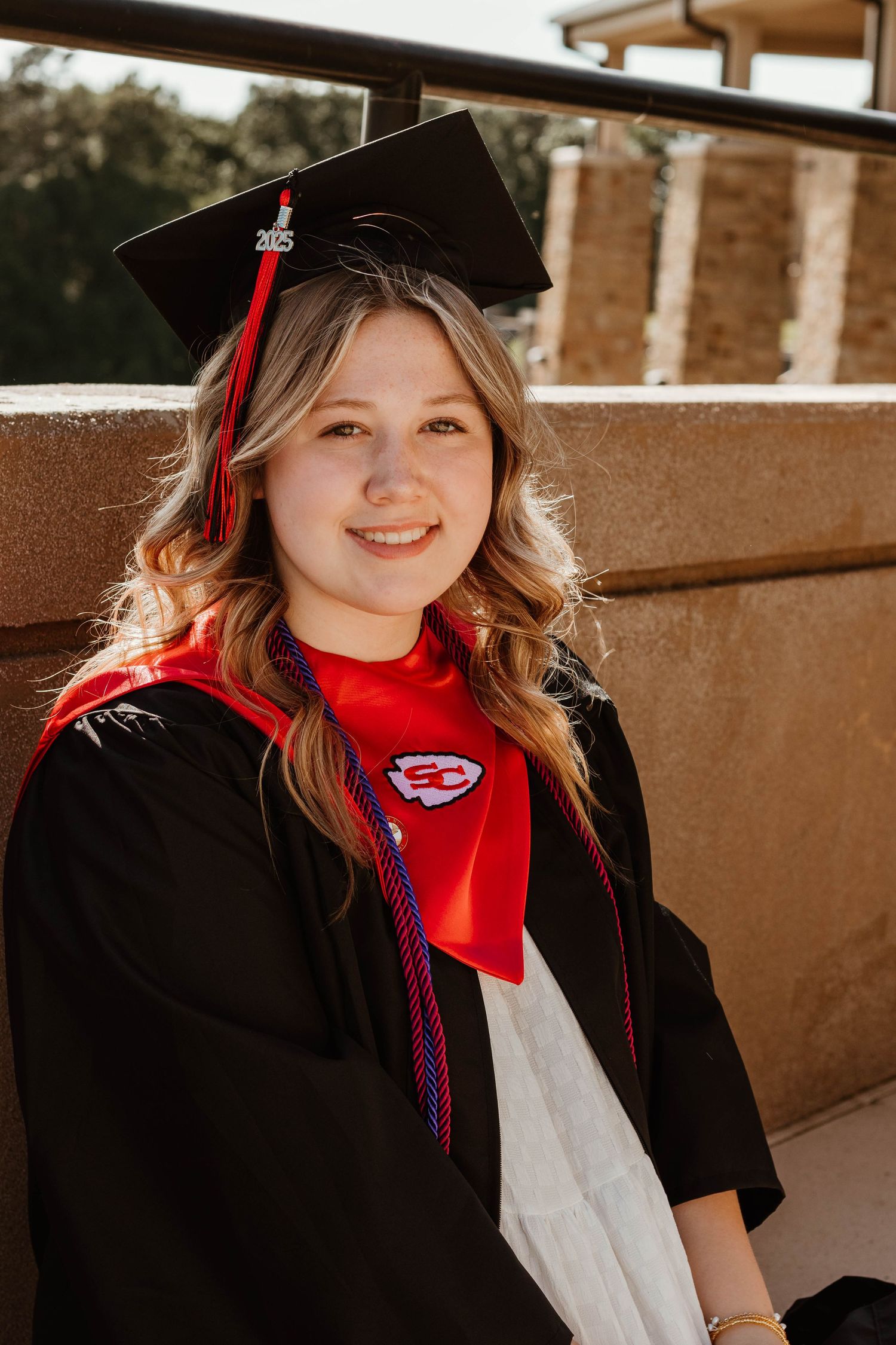 A graduate wearing academic regalia with a red scarf and Indians pin smiles at camera in Stephens County, Georgia.