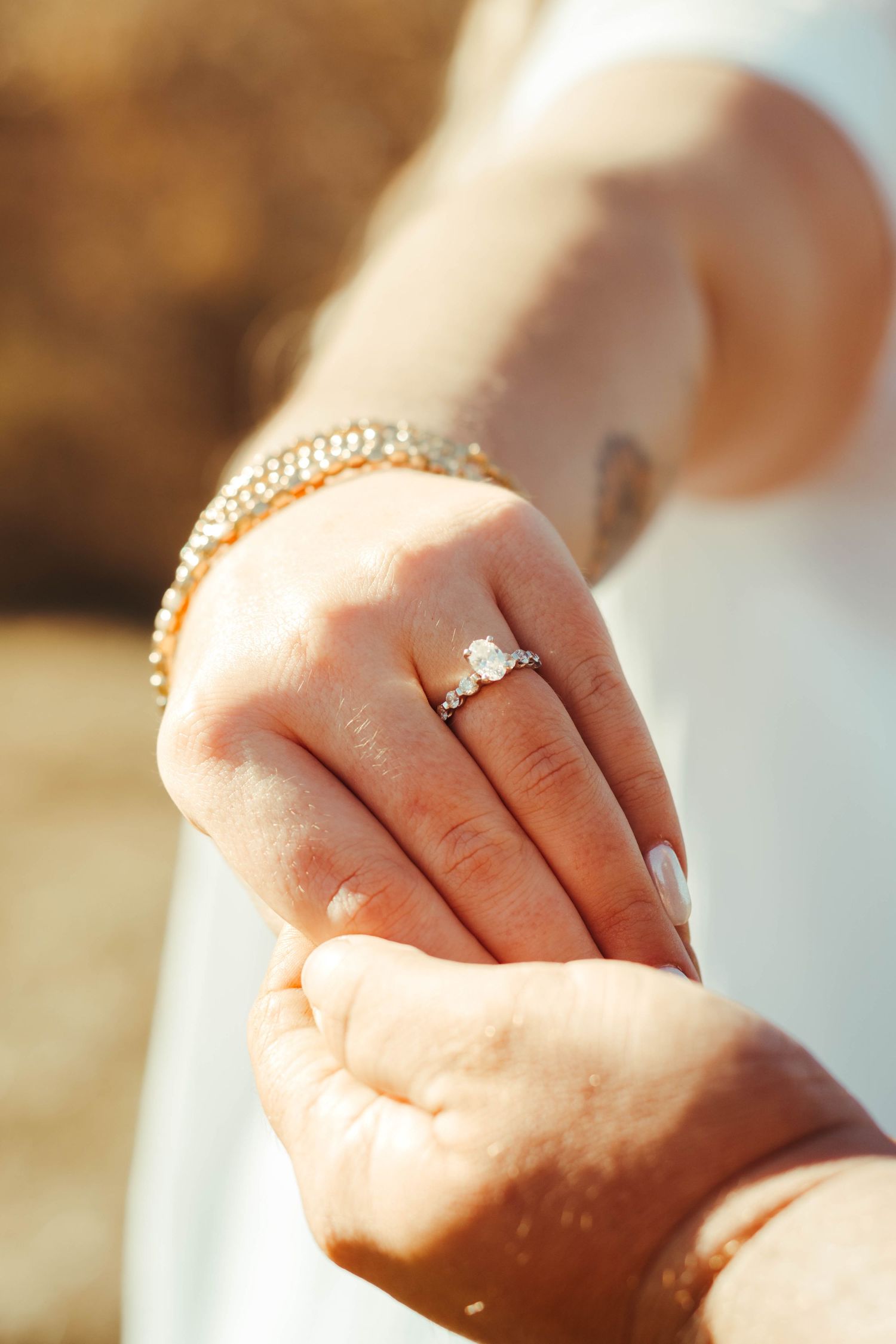 Close-up of a hand wearing an elegant diamond engagement ring with perfectly manicured nails in warm sunlight.