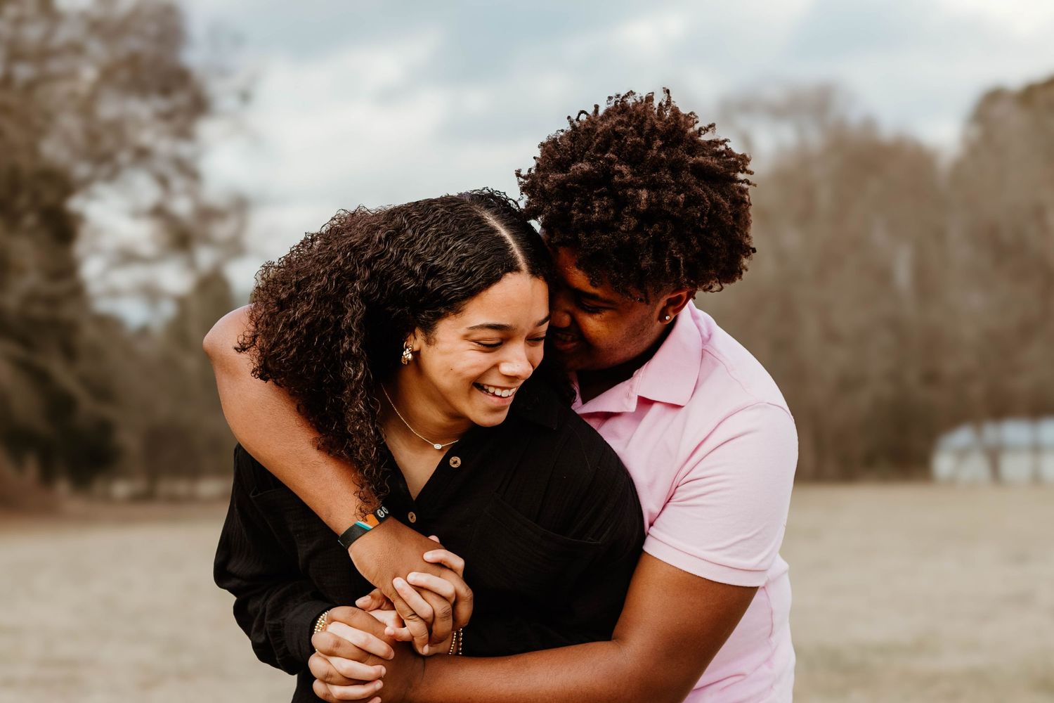 A couple shares a warm embrace and laugh together in a rustic outdoor setting at a farm in northeast Georgia.