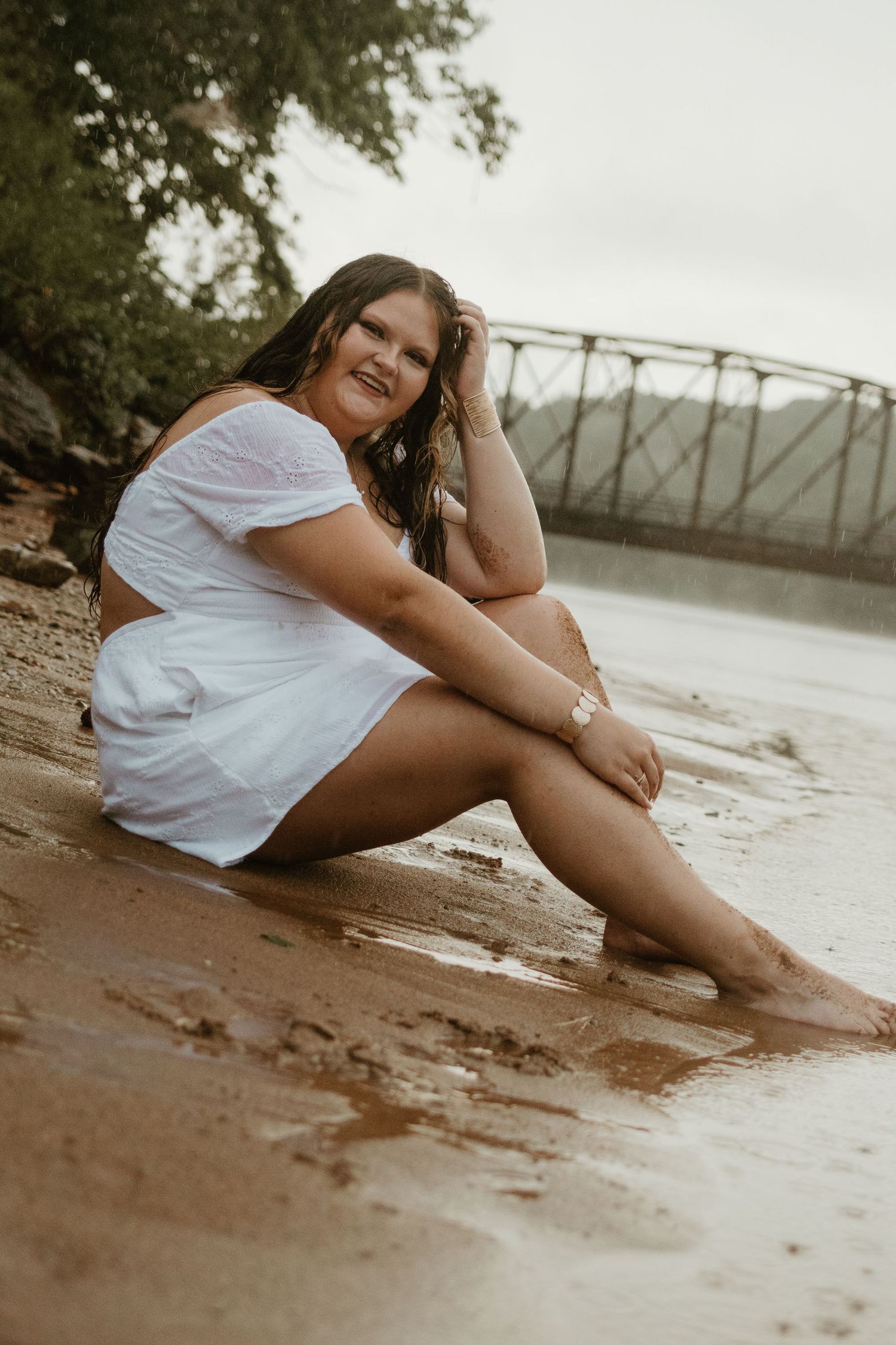 Person in white outfit sits casually on sandy lake beach during overcast day at Lake Hartwell.