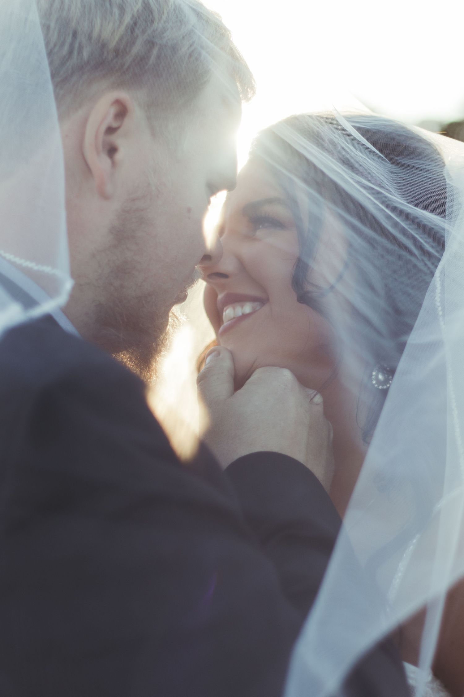 A romantic moment between newlyweds sharing a tender embrace under a veil with sunlight glowing behind them at their wedding in Toccoa, GA.