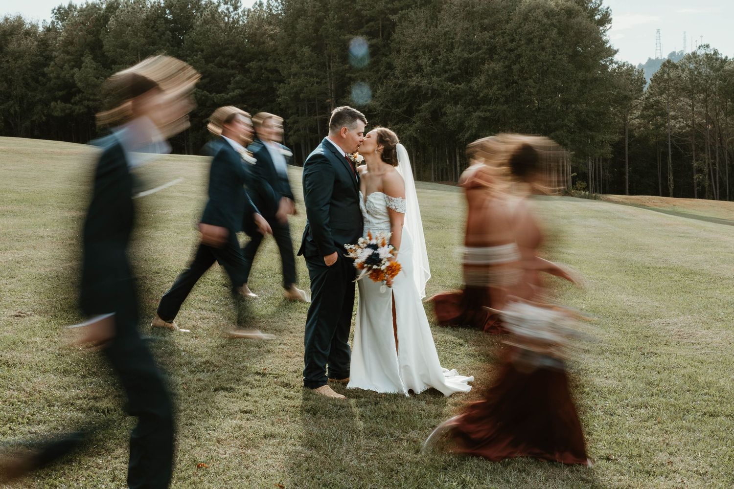 Wedding party runs playfully through a grassy field on an overcast day, creating a joyful candid moment.