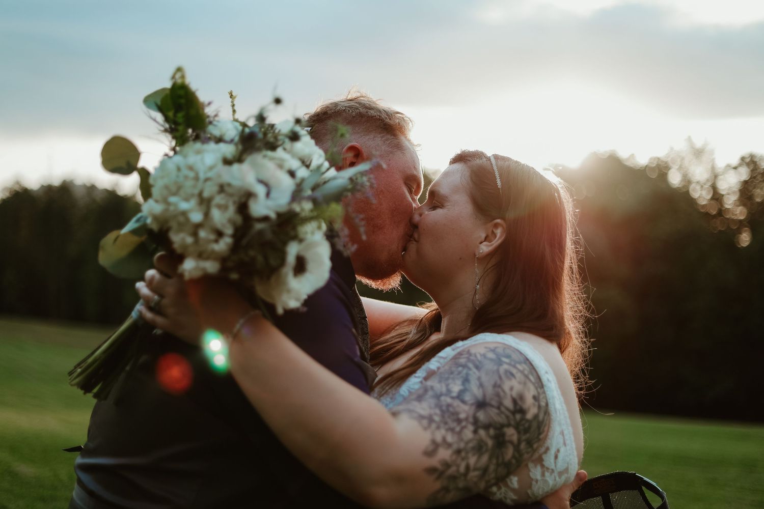 Golden hour wedding couple embraces among white floral bouquets in grassy field at a wedding venue in Toccoa, GA.