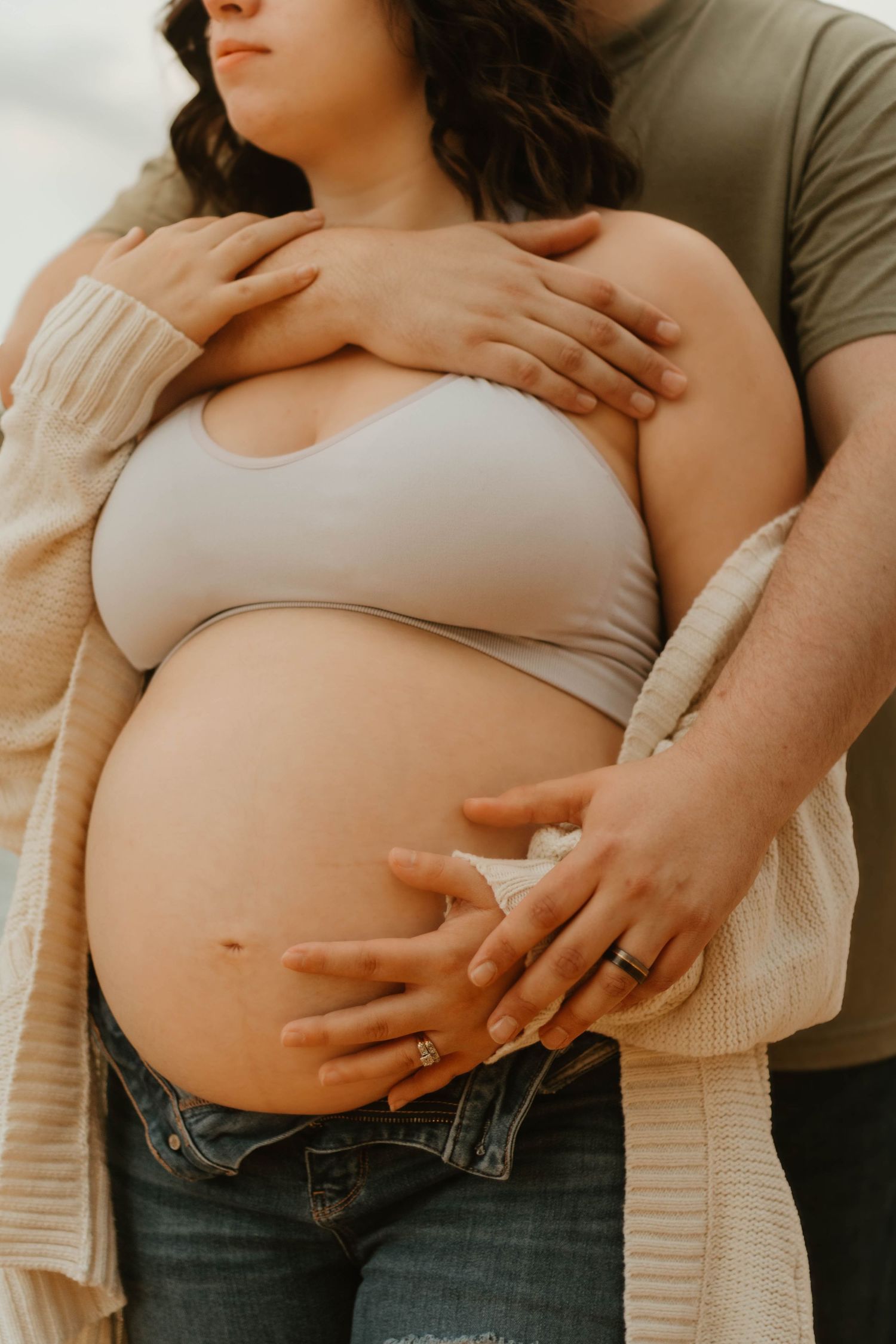 Intimate maternity photo showing couple's hands tenderly cradling pregnant belly in casual attire by Lake Hartwell in Northeast Georgia.