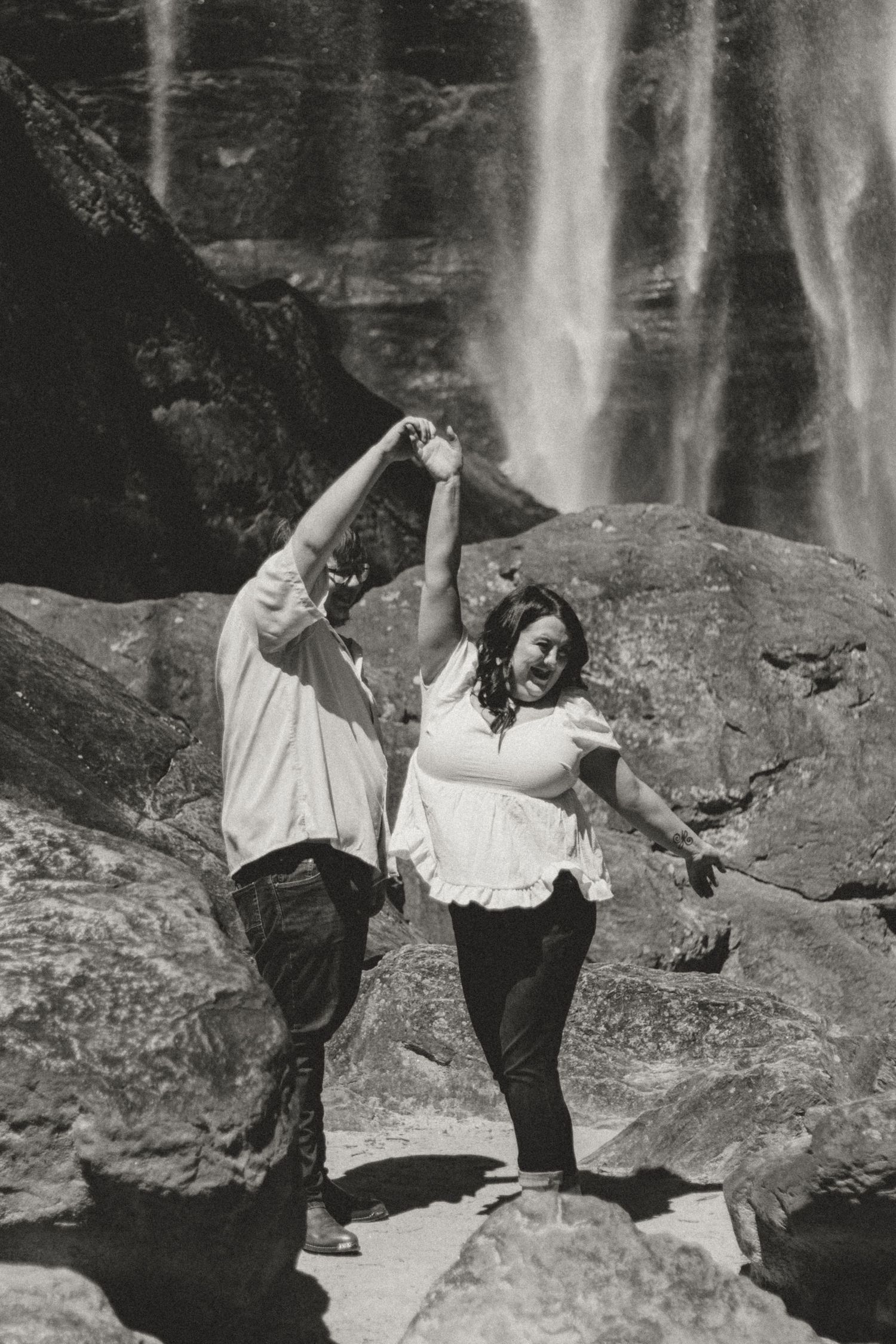 A person in vintage clothing strikes playful poses near a rocky cliff wall with a waterfall in the background.
