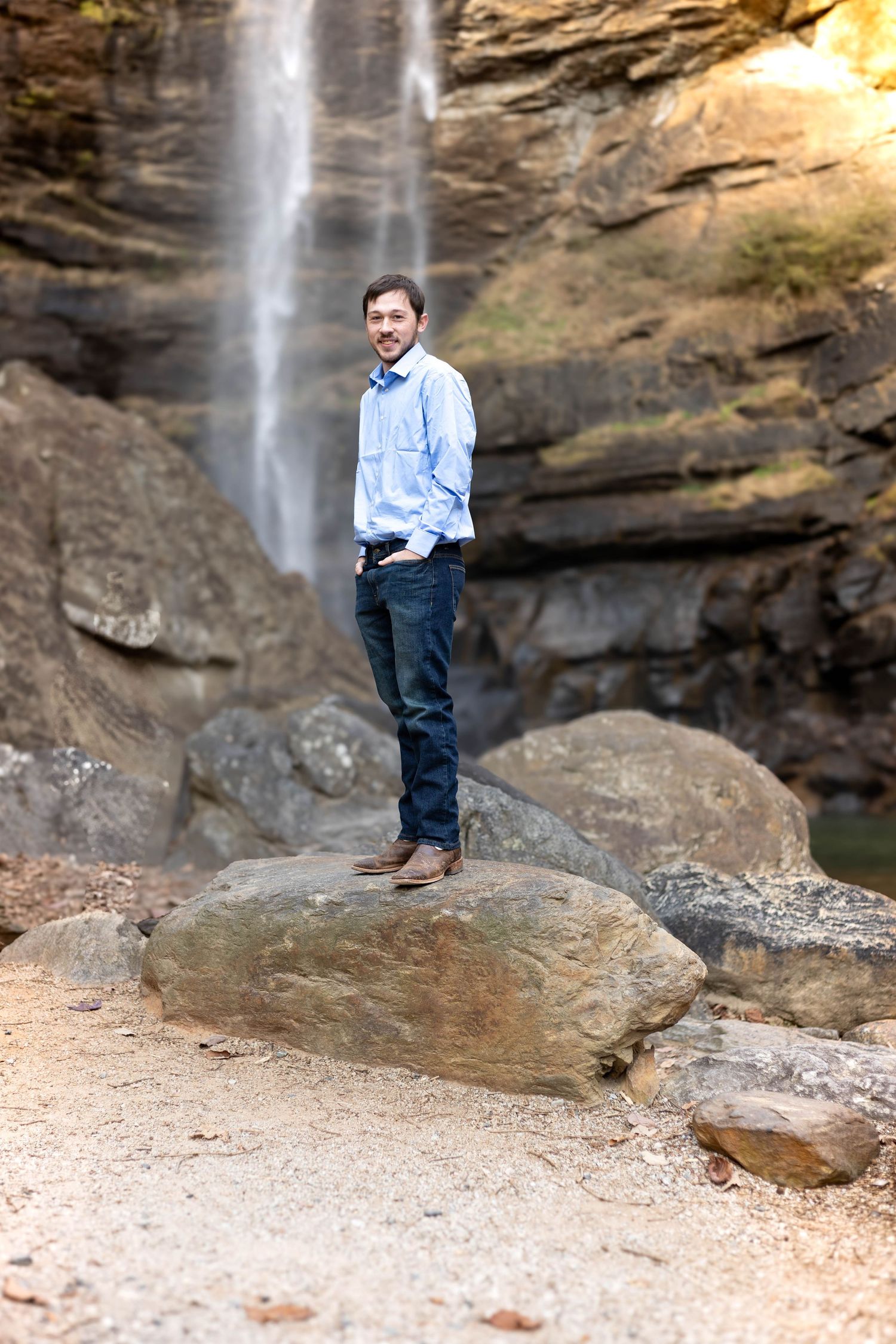 Casual portrait in light blue shirt against scenic waterfall and rocky cliff background at Toccoa Falls.