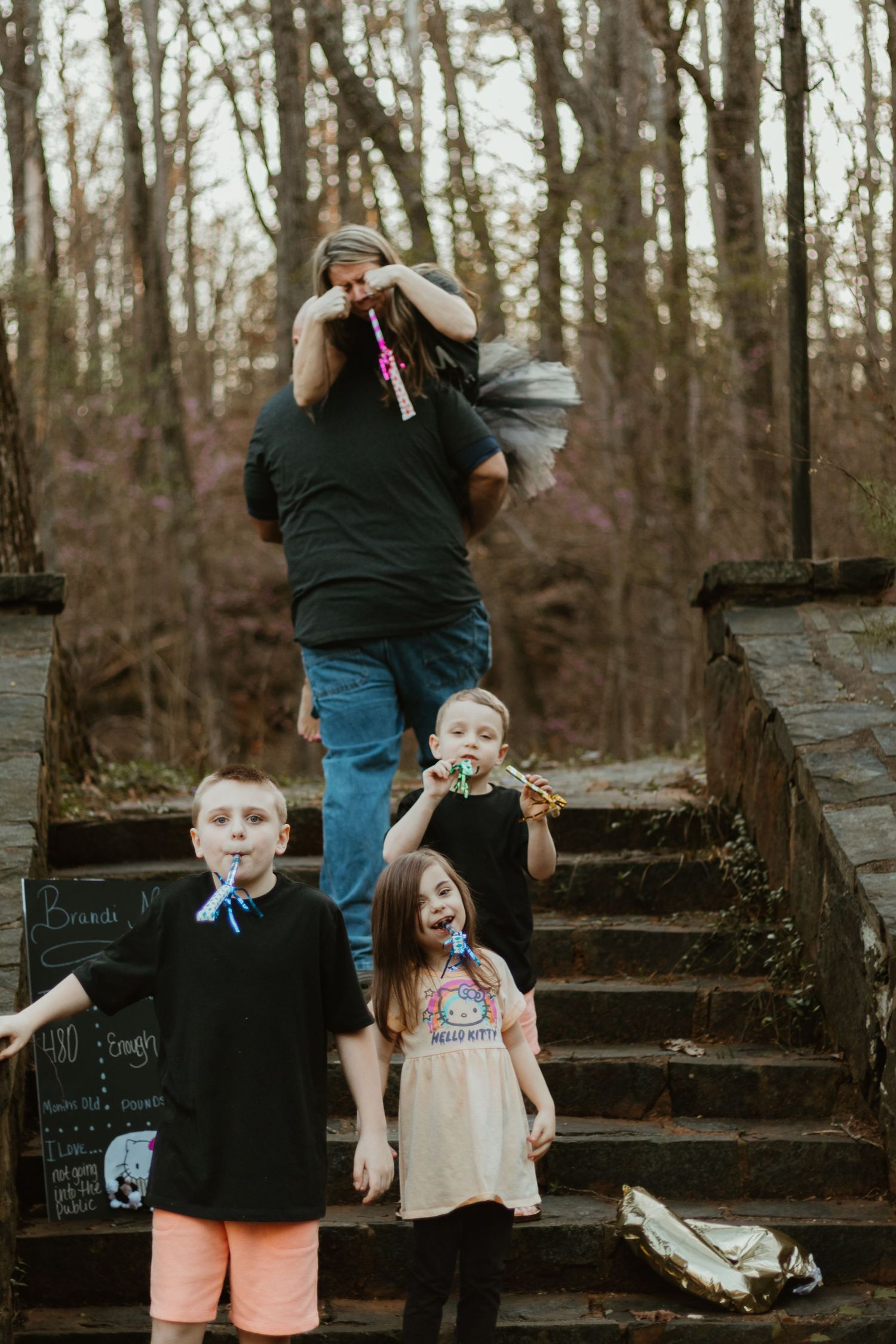 A family enjoys candid moments on a set of stone steps in a wooded area during a photo session.