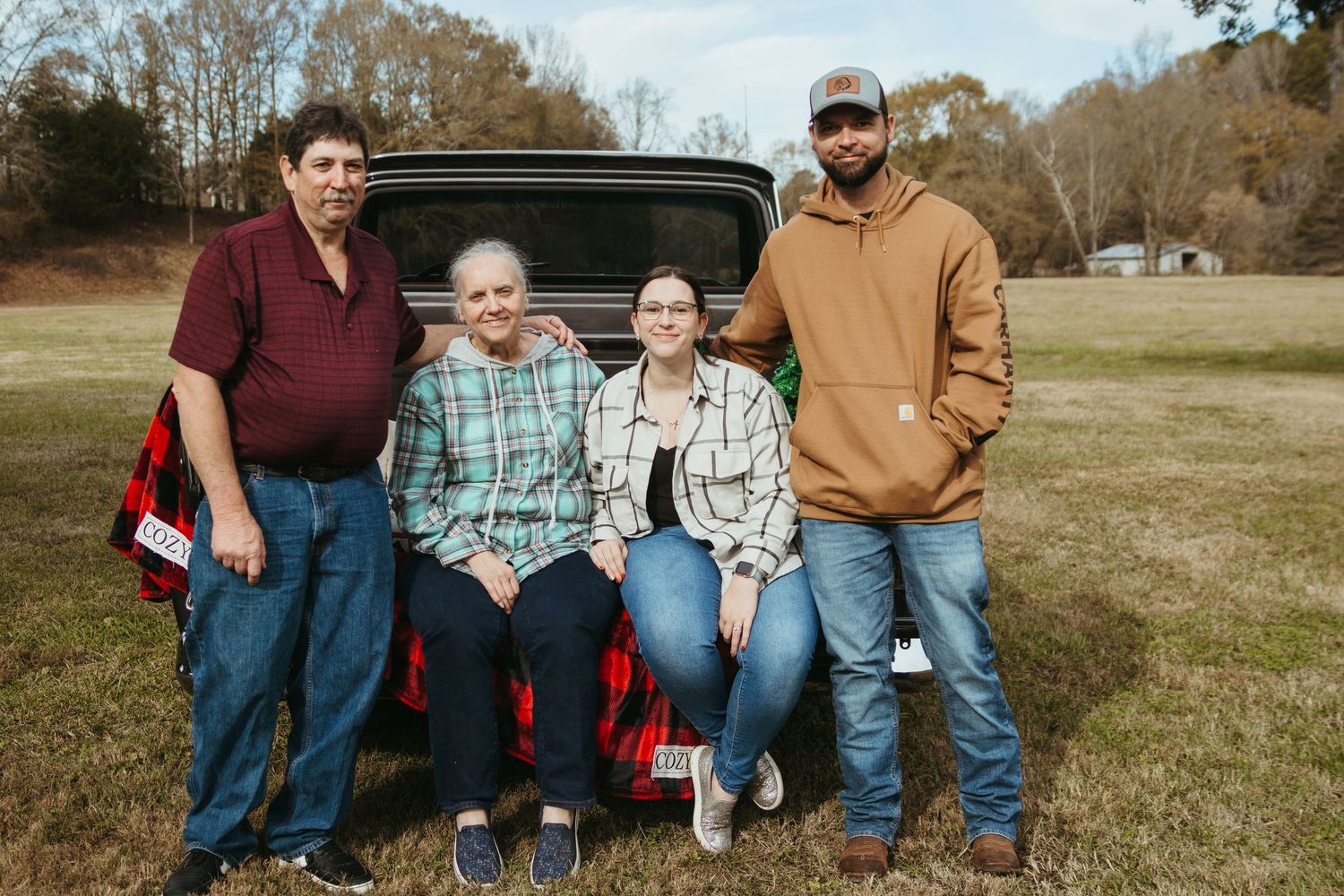 A group sits together on the tailgate of a pickup truck in a grassy field on an autumn day.