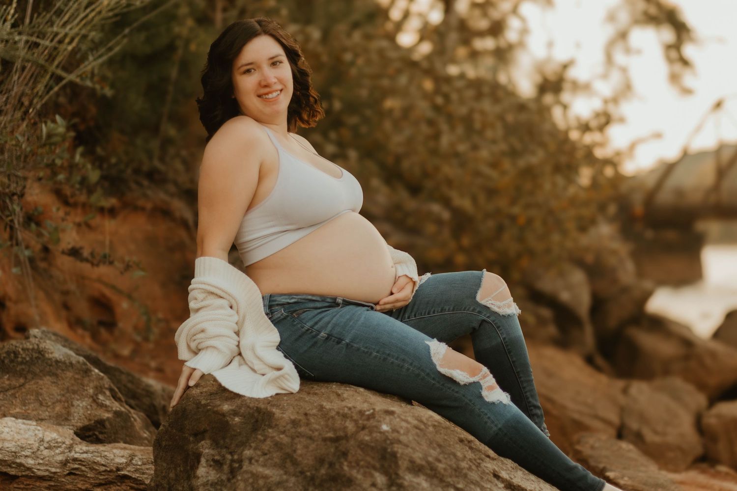 Maternity portrait on rocky shore with expecting mother in casual attire during golden hour at Broken Bridges on Lake Hartwell.