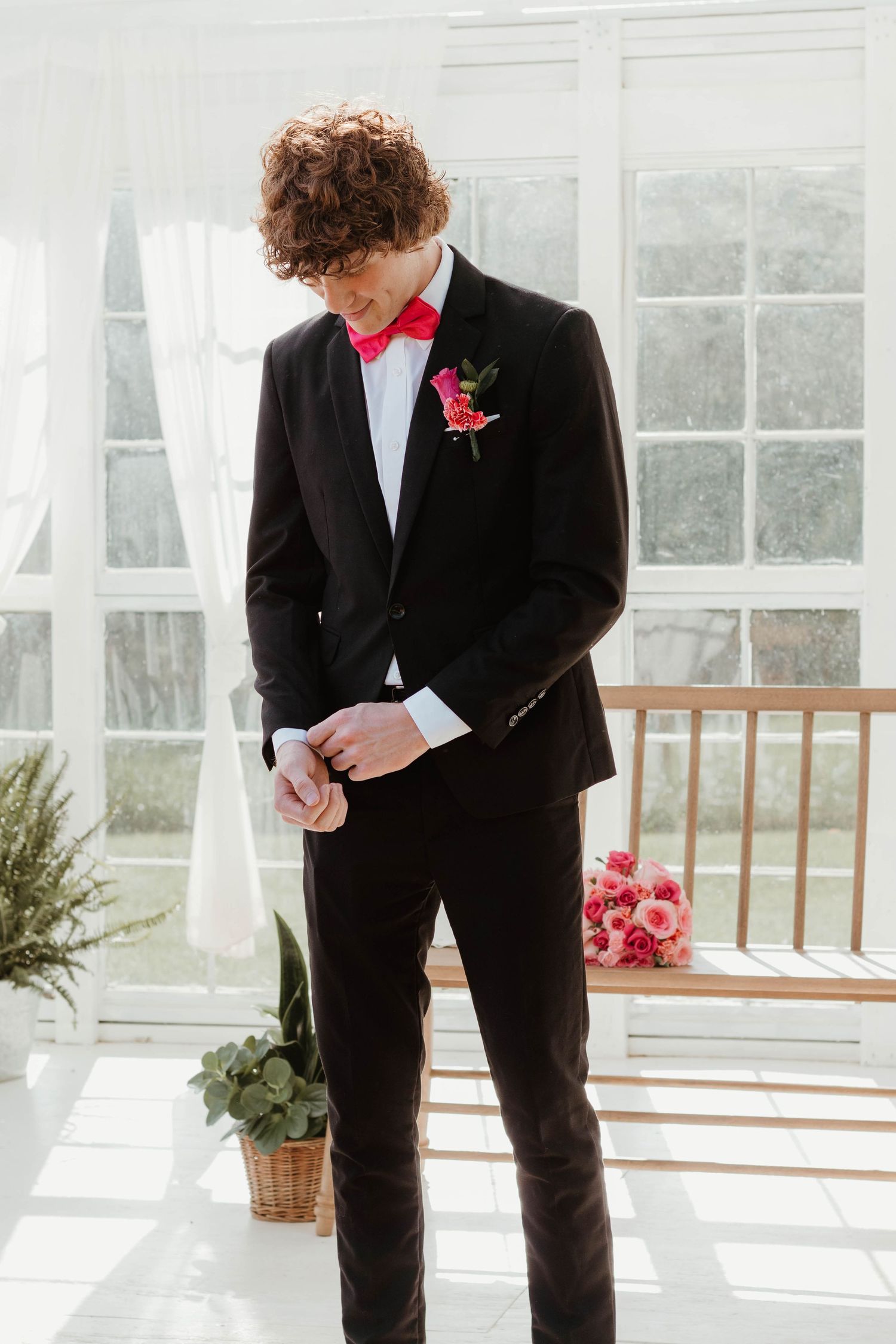 Formal fashion photo of a black tuxedo with pink bow tie and rose boutonniere in a bright greenhouse at The Farm at Daffodil Hill.