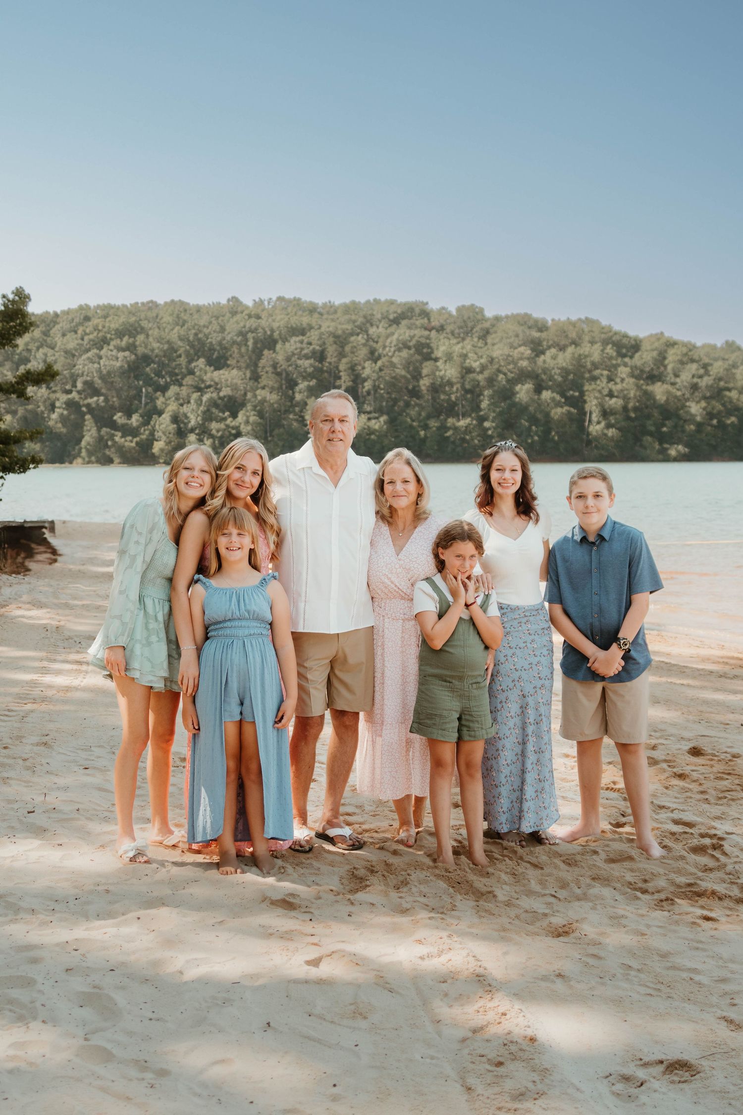 A group stands together on a sandy beach with trees and water in the background on a sunny summer day at Tugaloo State Park.